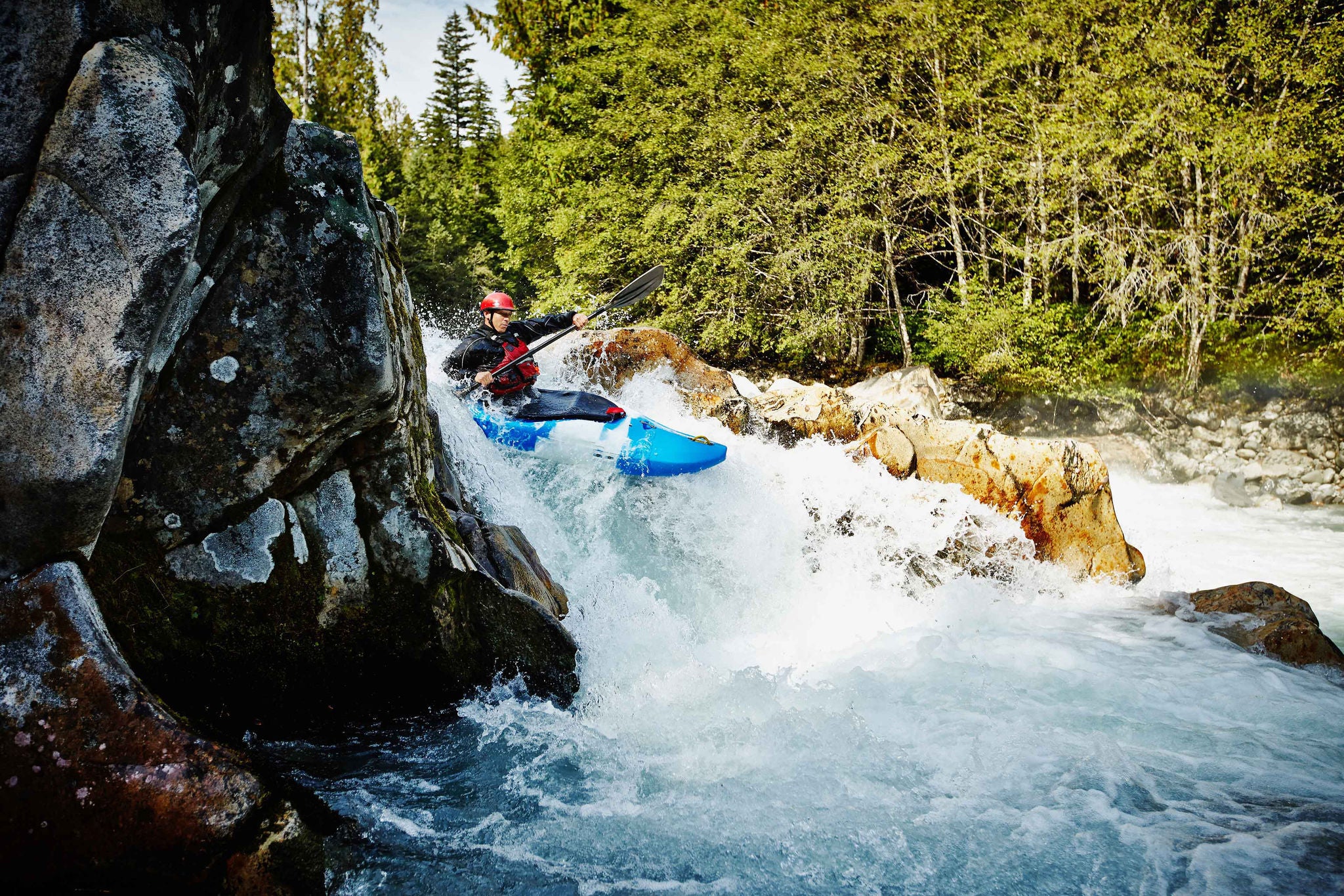 Man kayaking between rocks in white water rapids