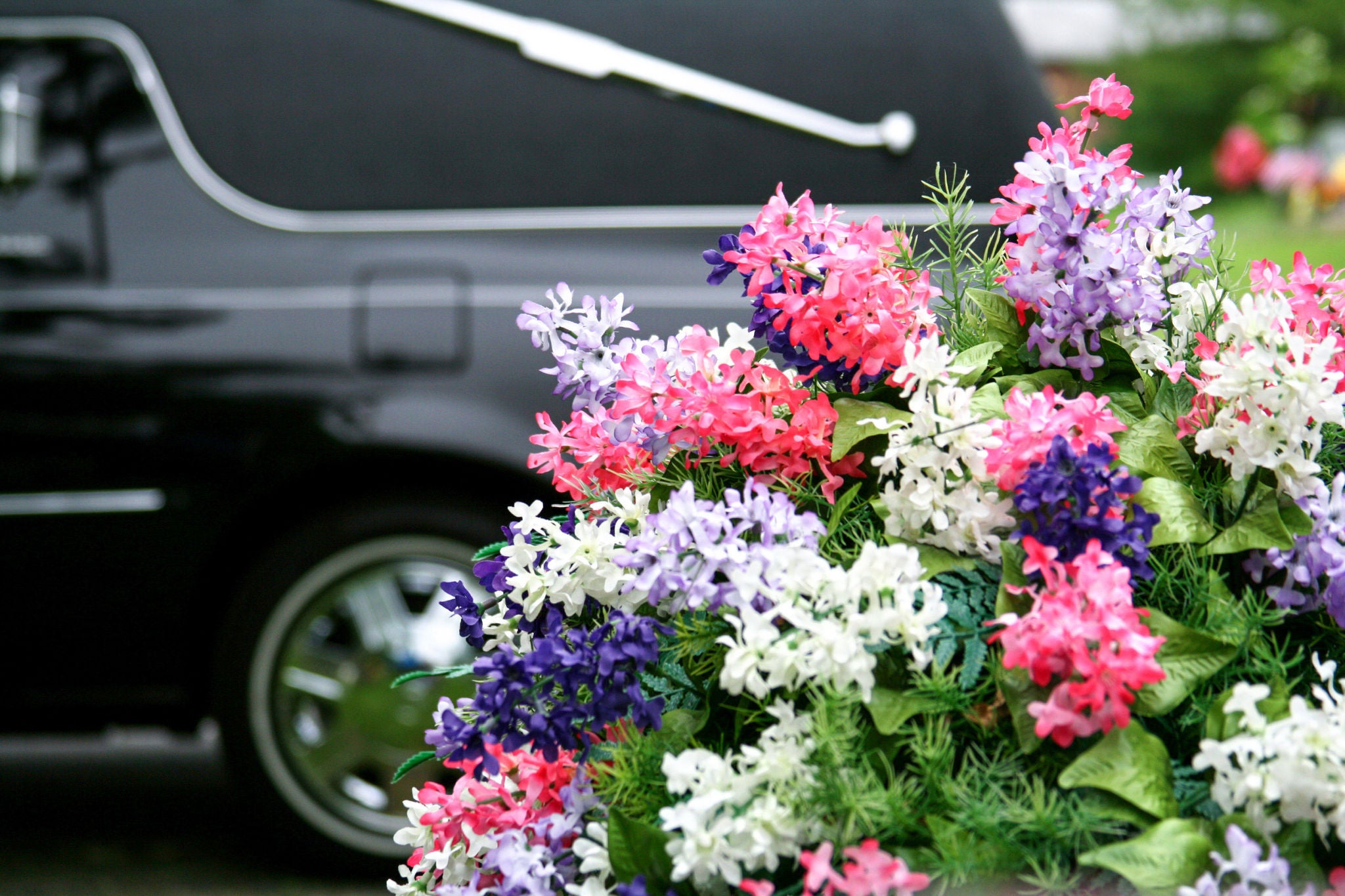 Nahaufnahme von einem Trauergesteck vor einem unscharfen Leichenwagen