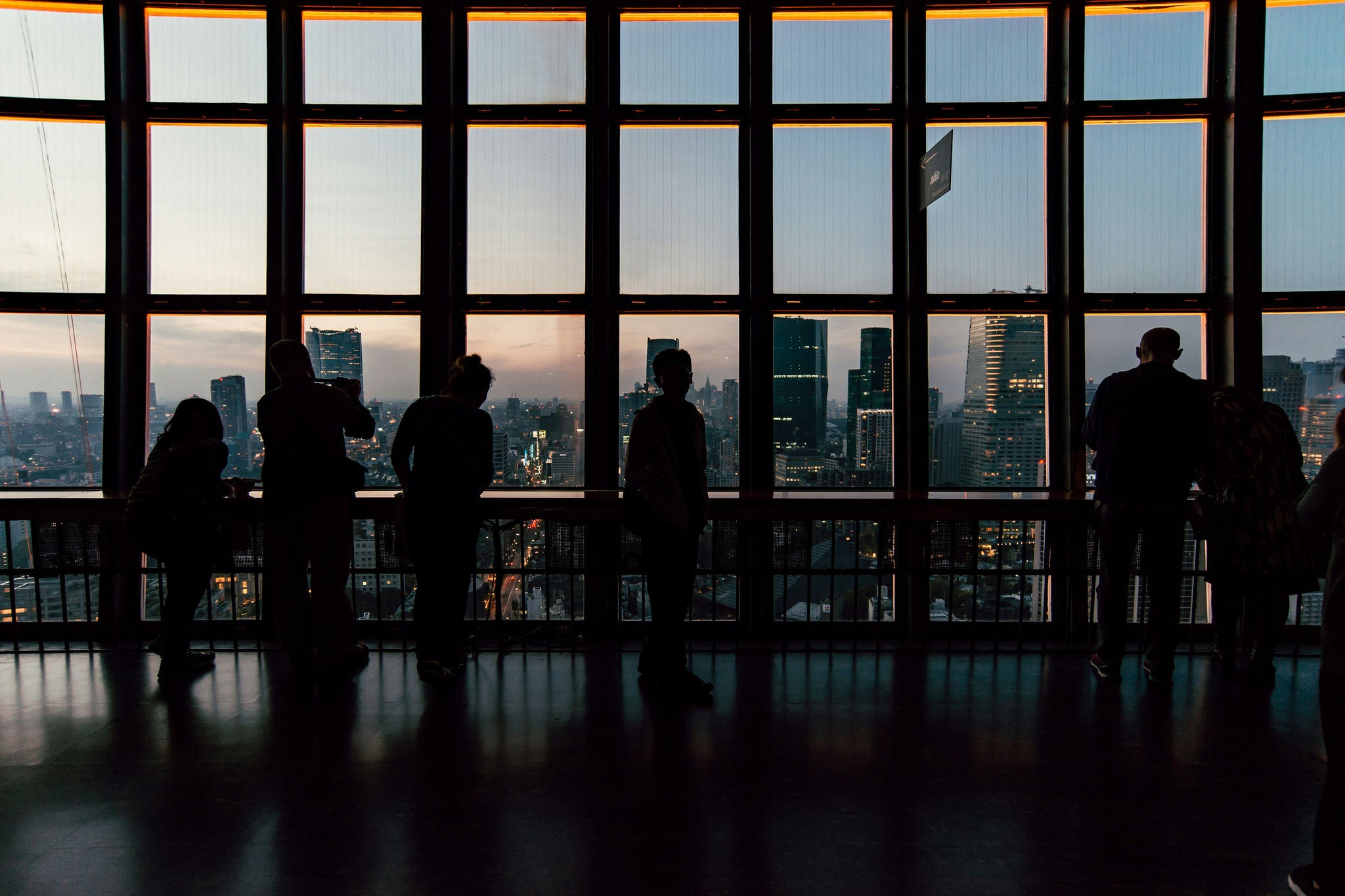 People standing by large windows looking at a city view at sunset