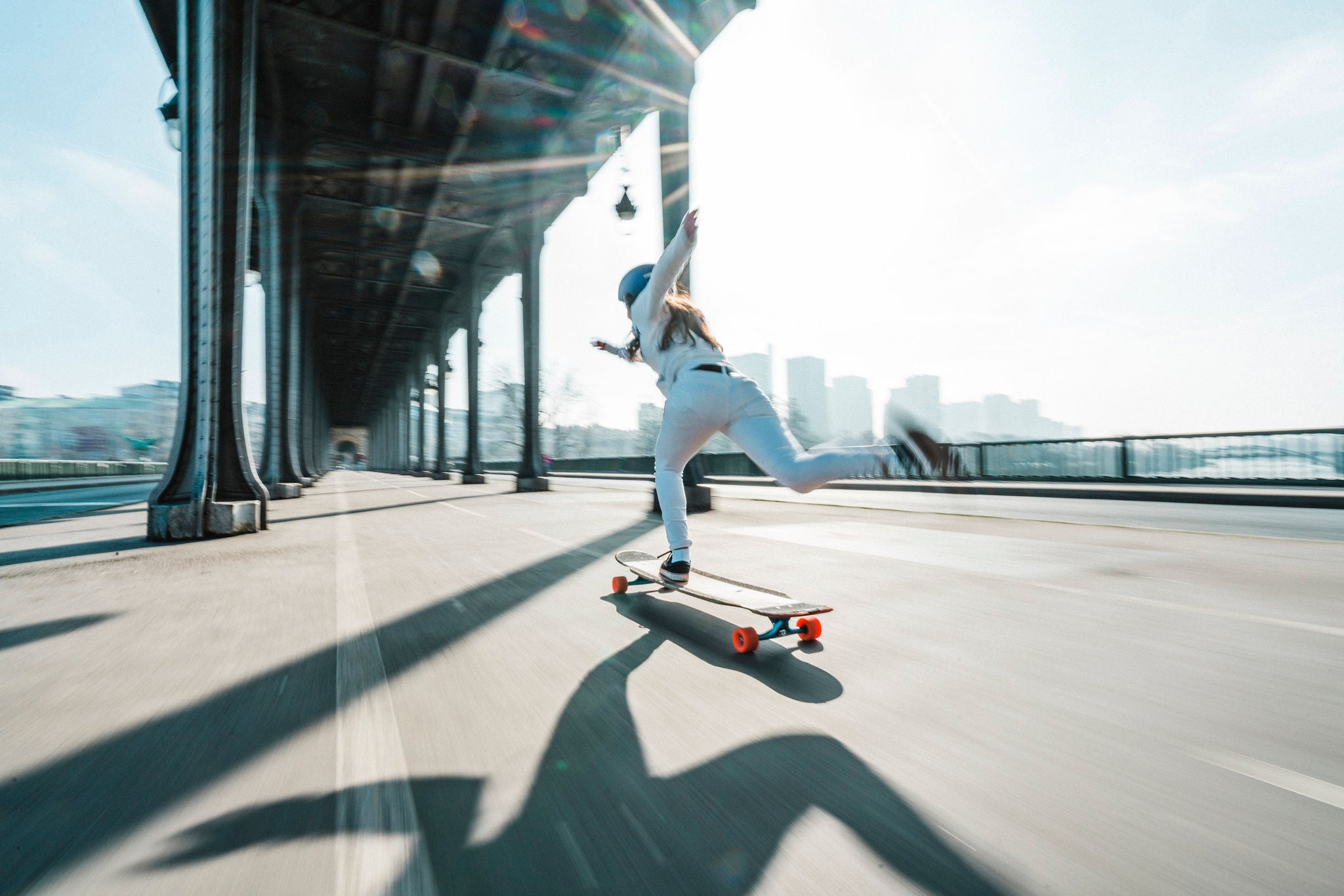 Woman skateboarding under bridge city against sky