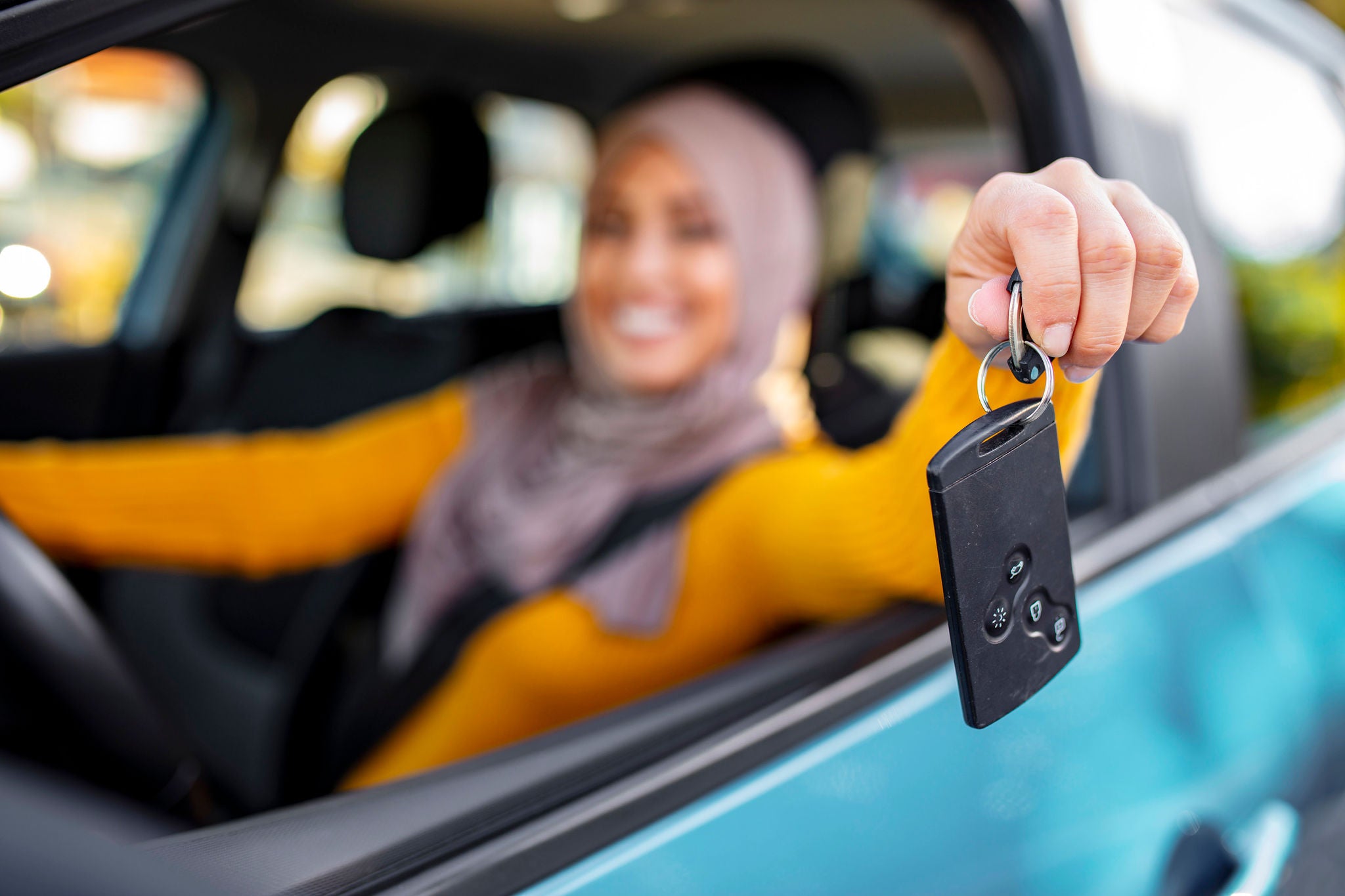 Happy arabian woman holding car key in new vehicle. Muslim woman in her new car. Happy arabian woman holding car key inside new vehicle. Muslim Woman Sitting In Car