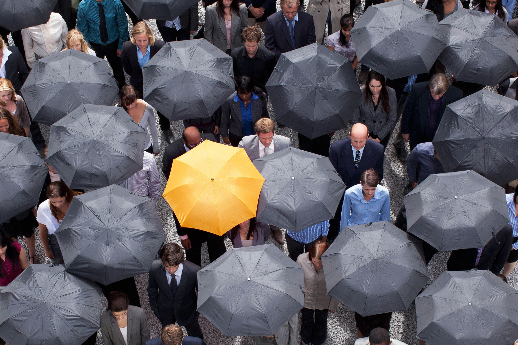 Yellow umbrella standing out in crowd of business people