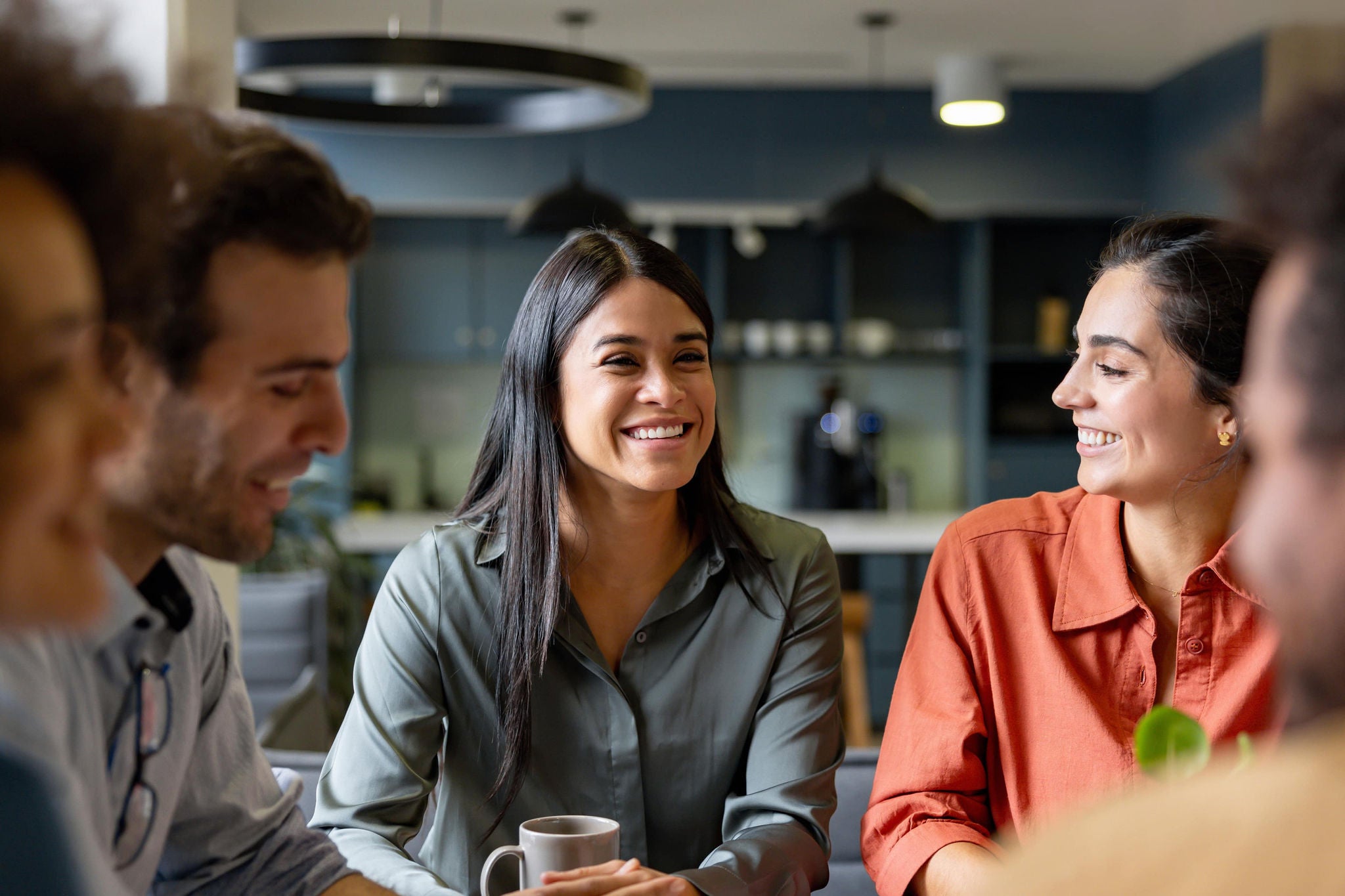 A smiling young woman with headphones and folders, standing outdoors on a college campus.