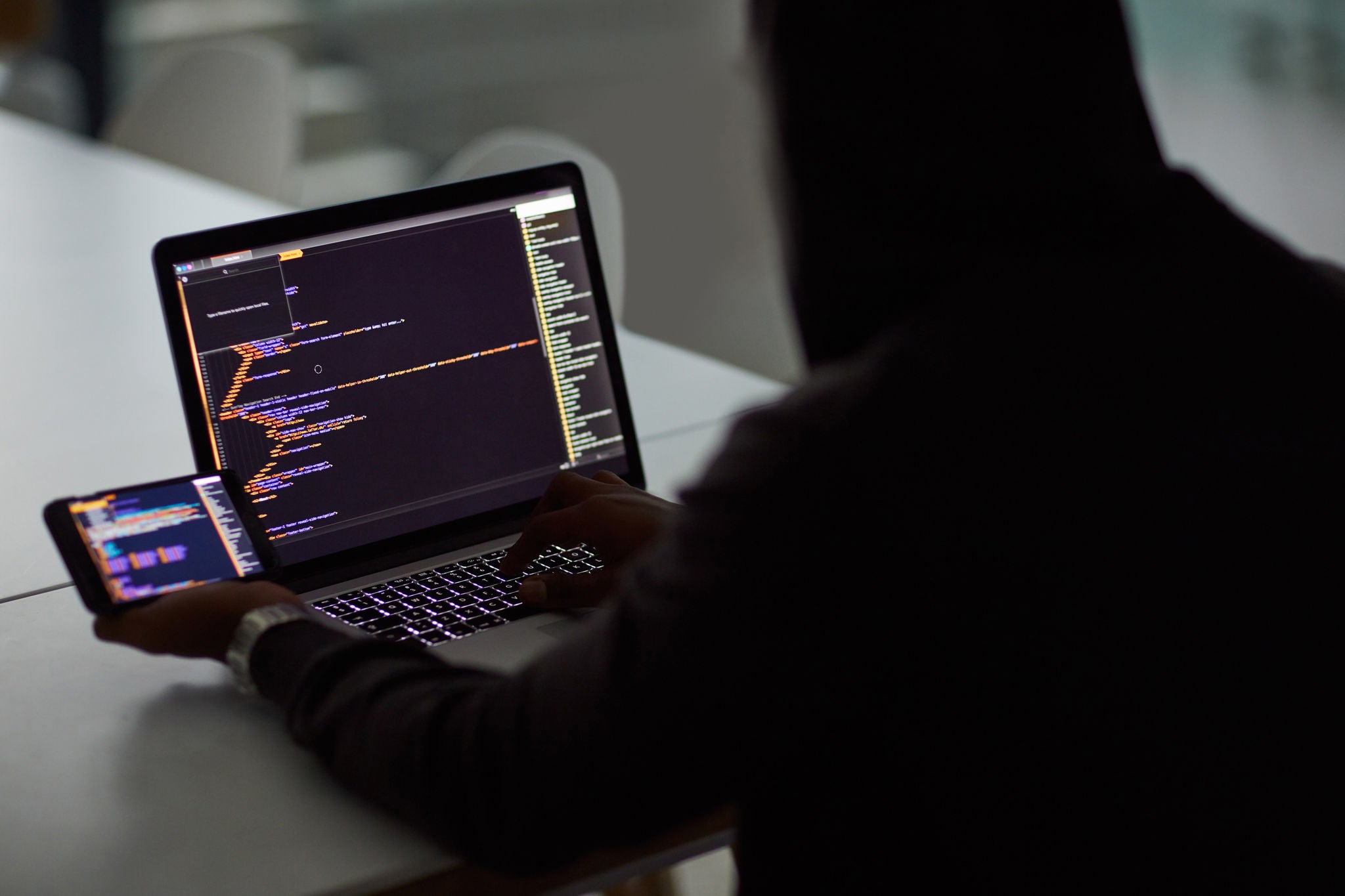 Shot of an unrecognisable hacker using a laptop and smartphone