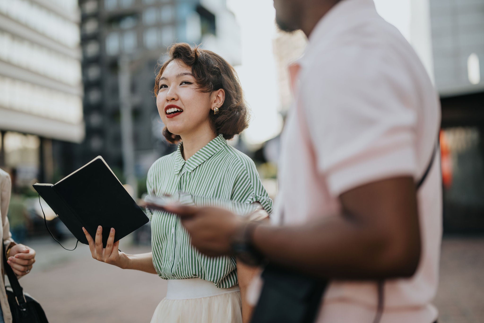 Asian woman holding an open notebook while standing outdoors with colleagues