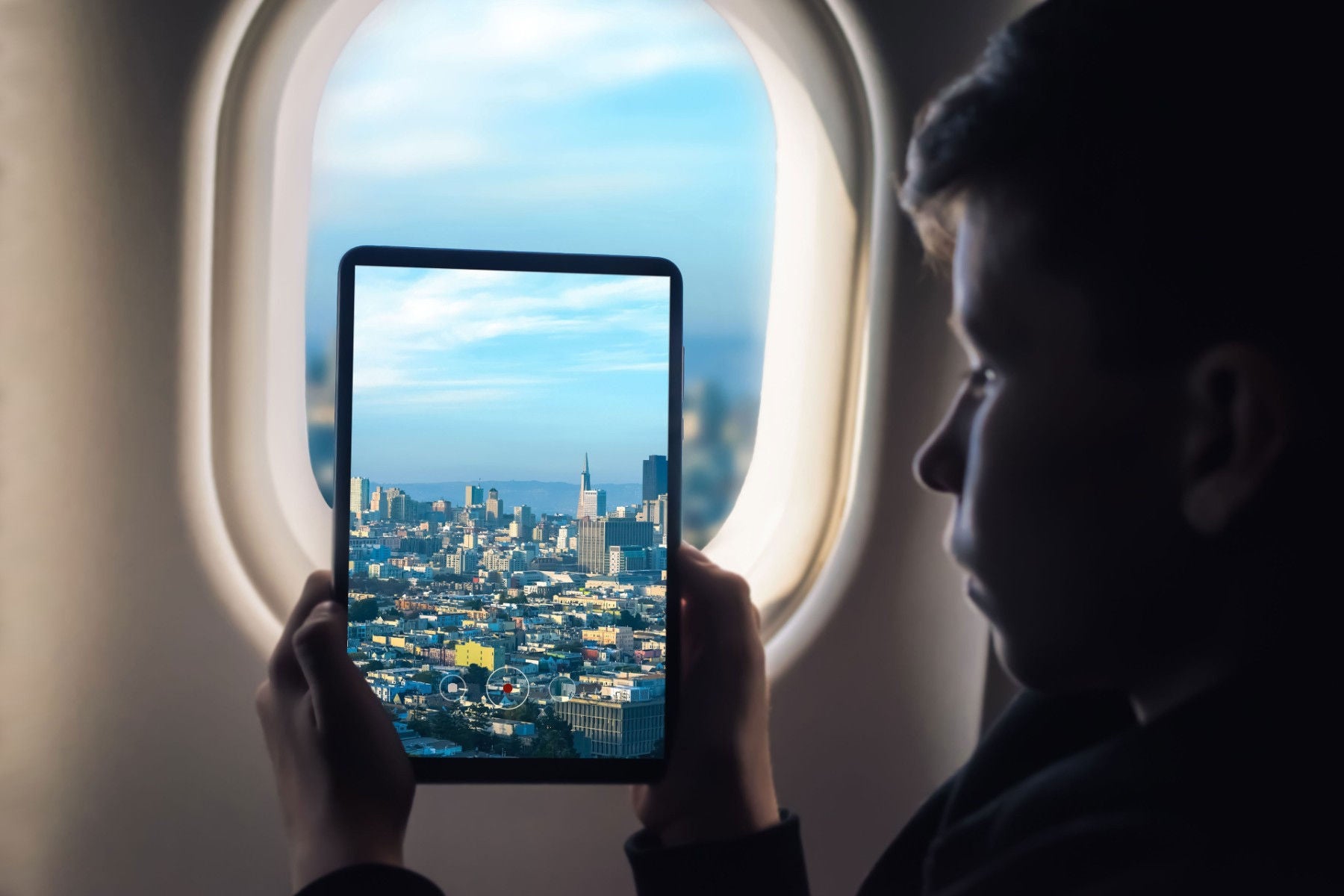 Boy taking picture on a tablet from inside of an airplane