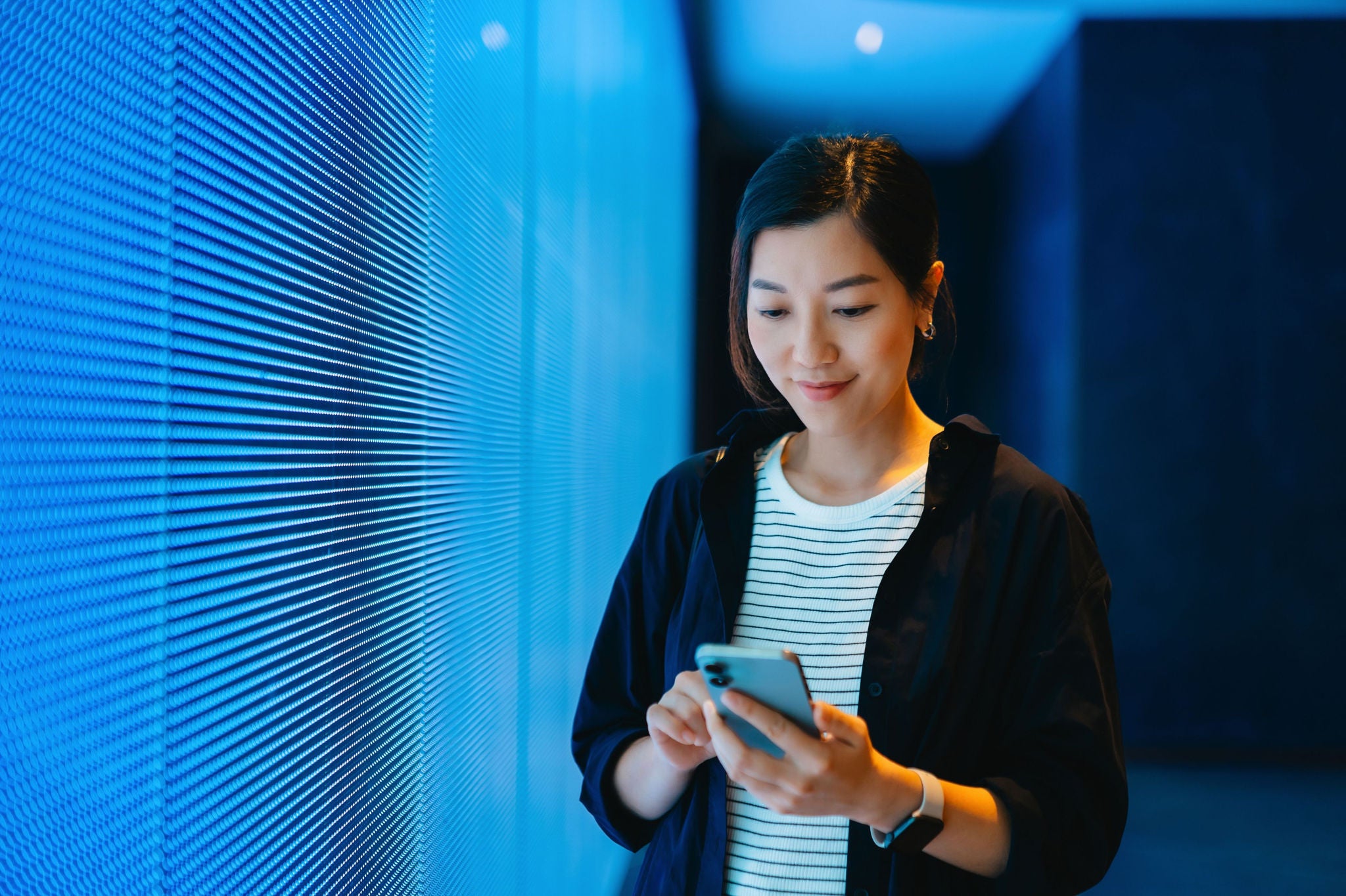 Asian woman using smartphone against LED digital display screen