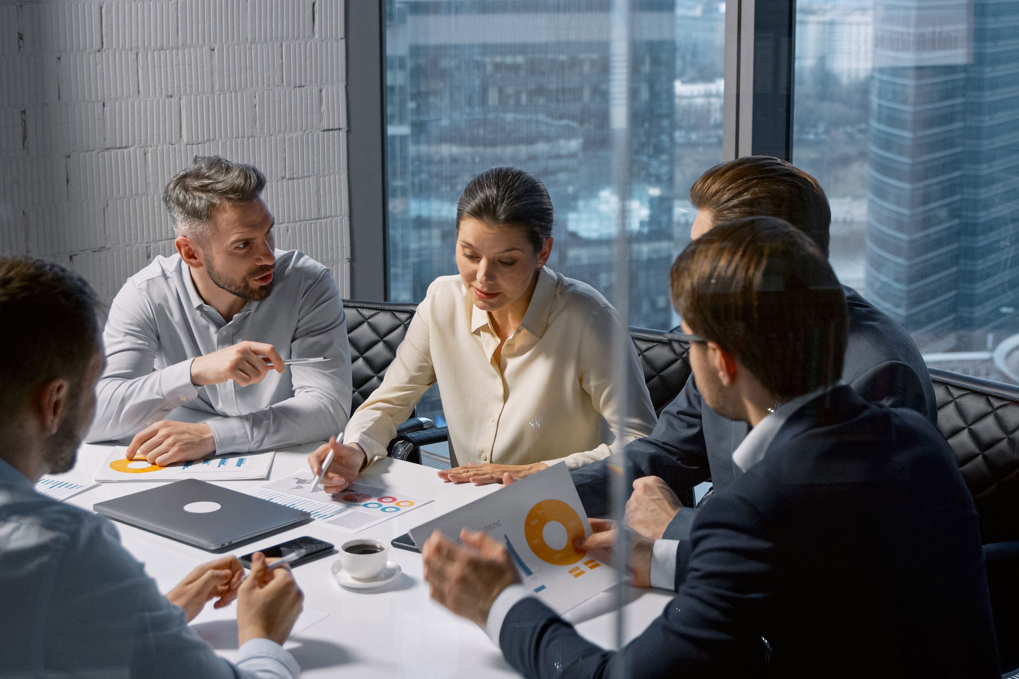 Corporate businesswoman communicating with team while sitting at desk in meeting room in office