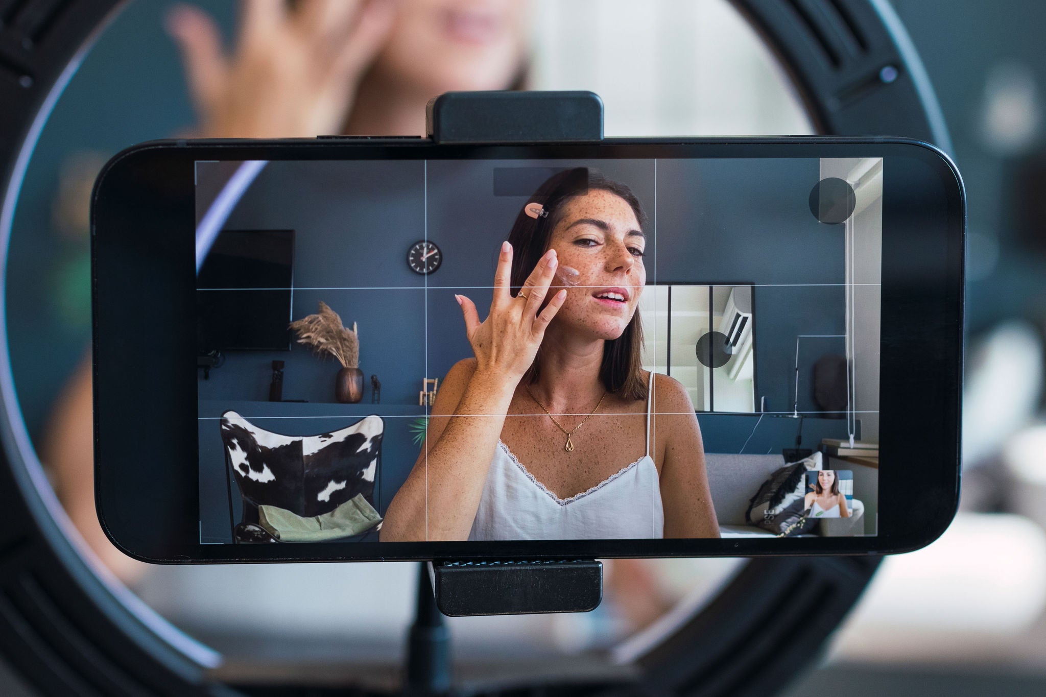 Jonge vrouw neemt een vlog op met haar smartphone terwijl ze huidverzorging aanbrengt
