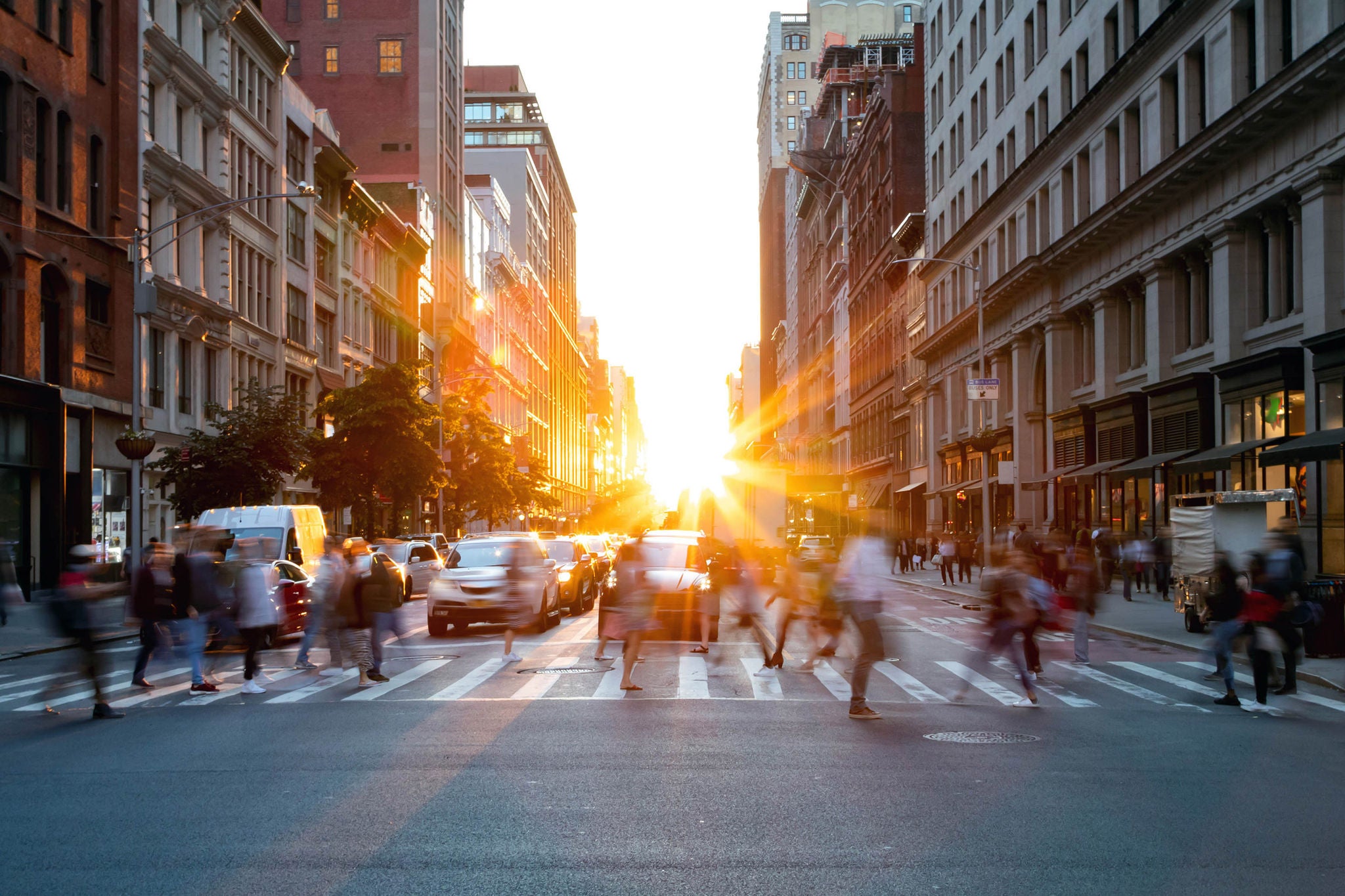 Crowds of busy people walking through the intersection of 5th Avenue and 23rd Street in Manhattan, New York City with bright sunset background