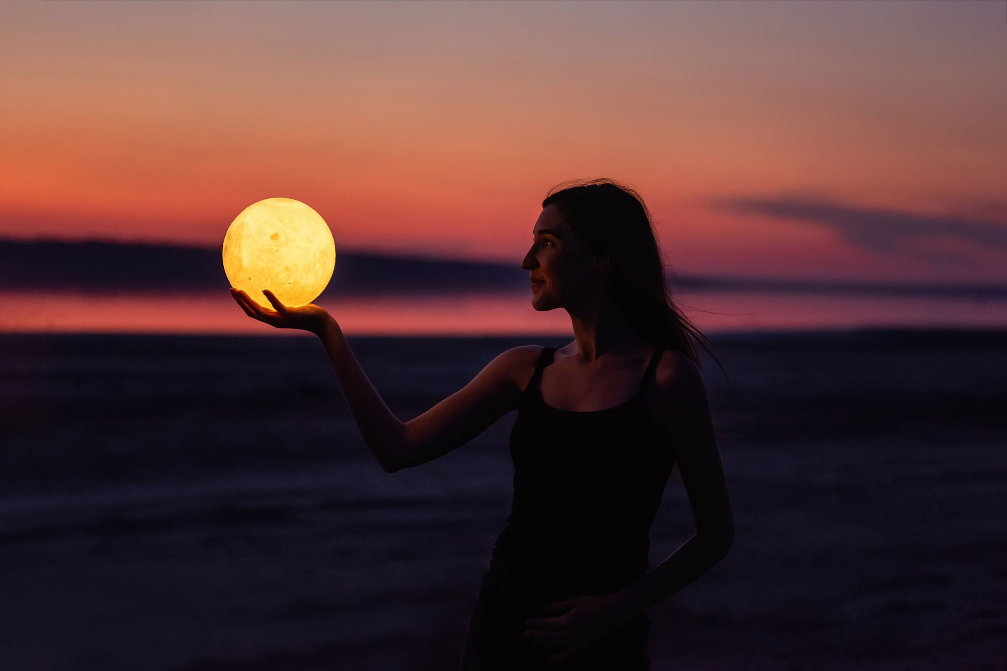 A young woman holds a moon lamp in her hand on a beach
