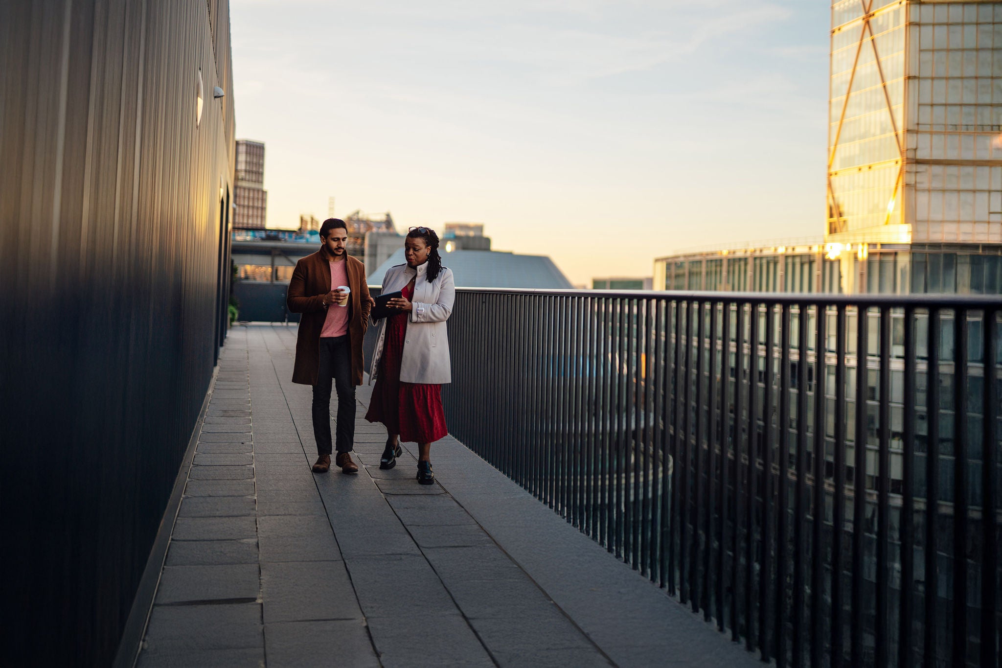 Mixed race businessman talking with an African businessman on city sidewalk. Multiracial business team working on digital tablet at rooftop garden in a high-rise office building. They're talking, planning and thinking strategy and discussing business strategy at urban balcony overlooking city, Liverpool, London.