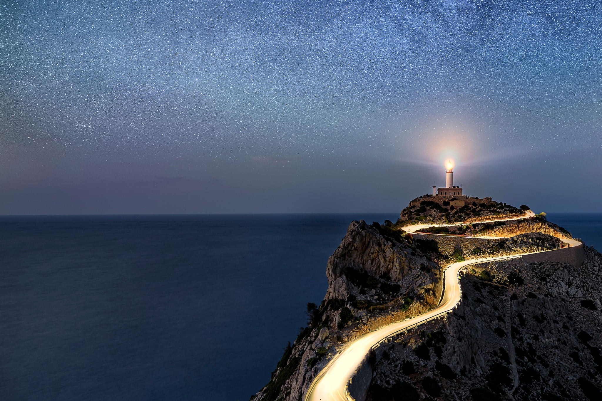 Phare sur falaise rocheuse route sinueuse sous ciel etoile