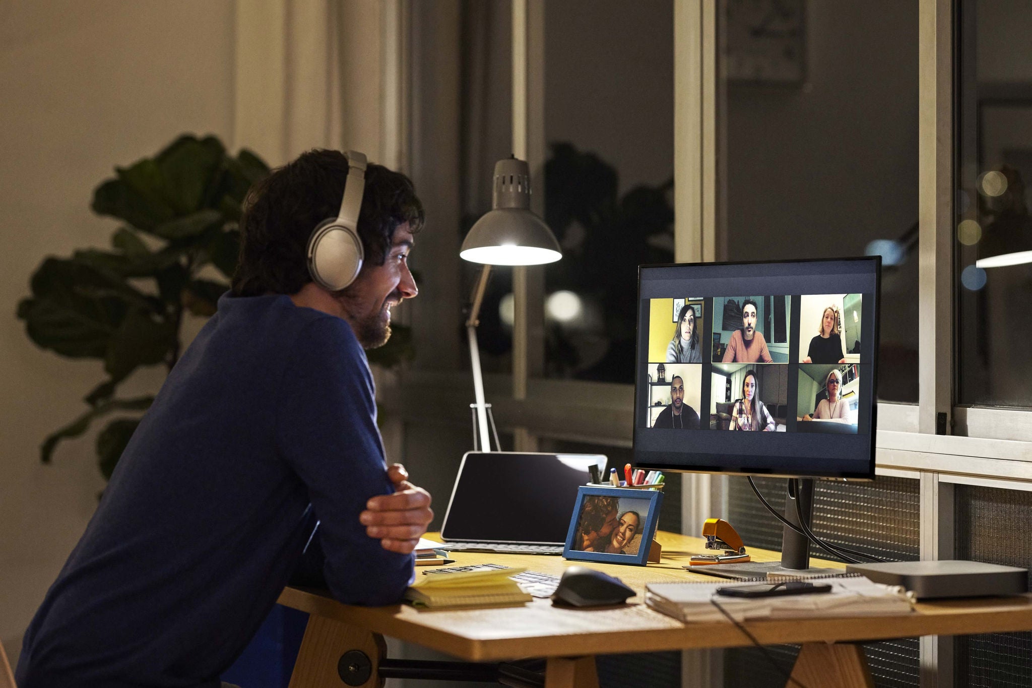 Side view of male freelance worker discussing during video call with colleagues. Smiling businessman is sitting at table in home office. He is working late at night.