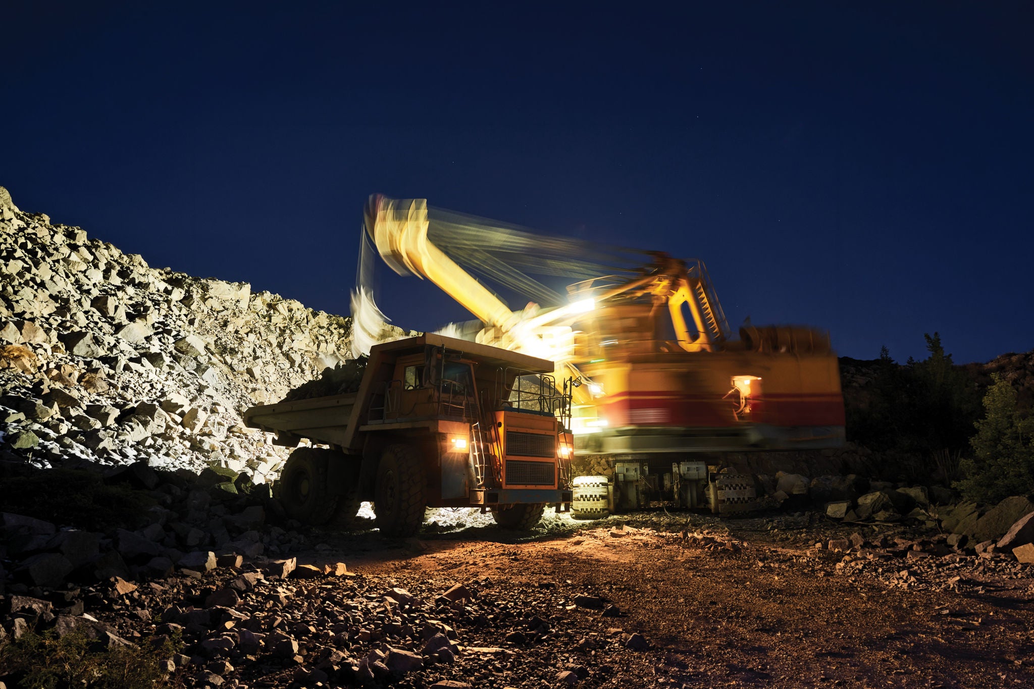 Excavator loading rock into a haul truck at a quarry site during nighttime operations