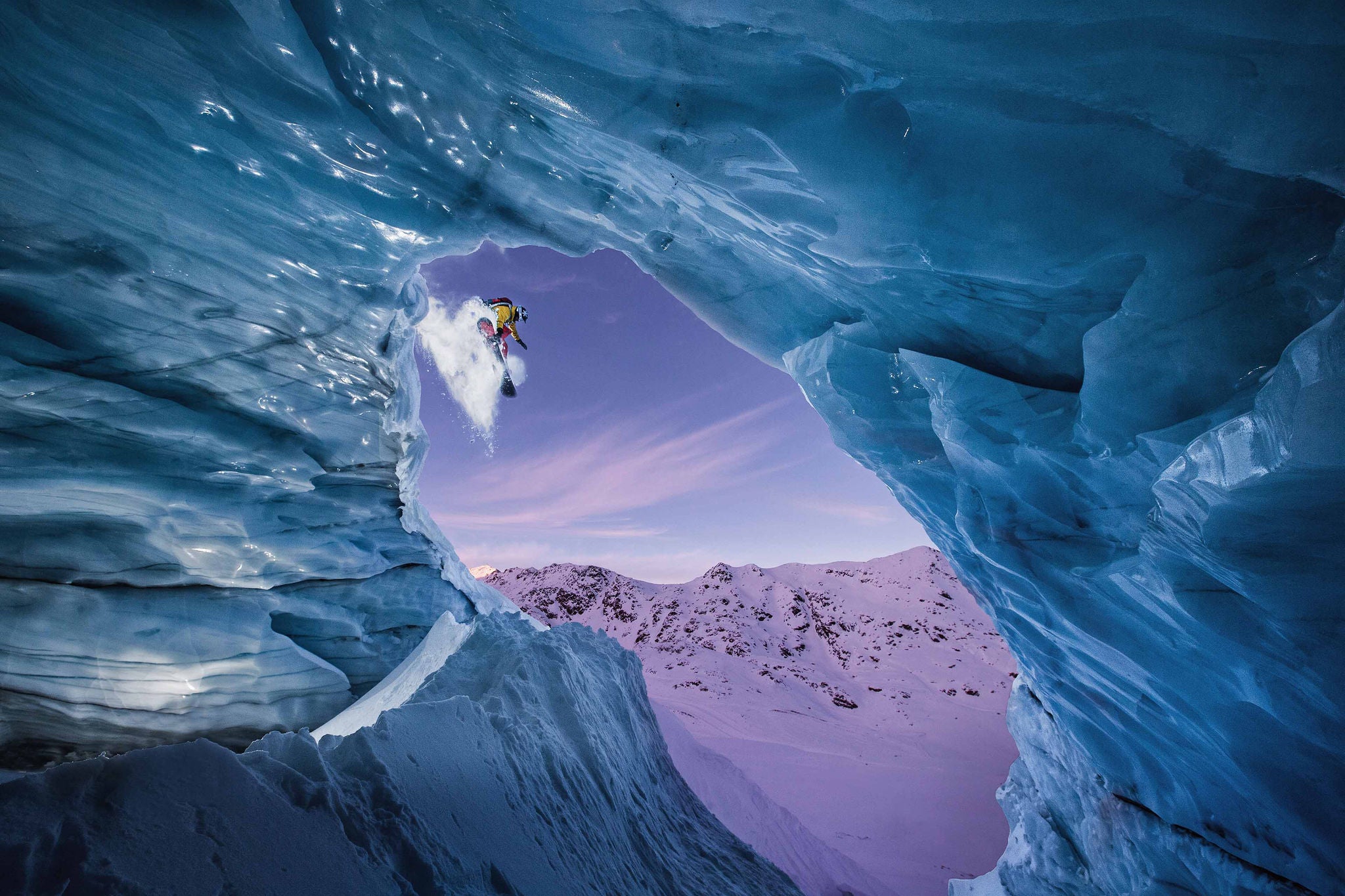 Male snowboarder jumping down from a glacier cave