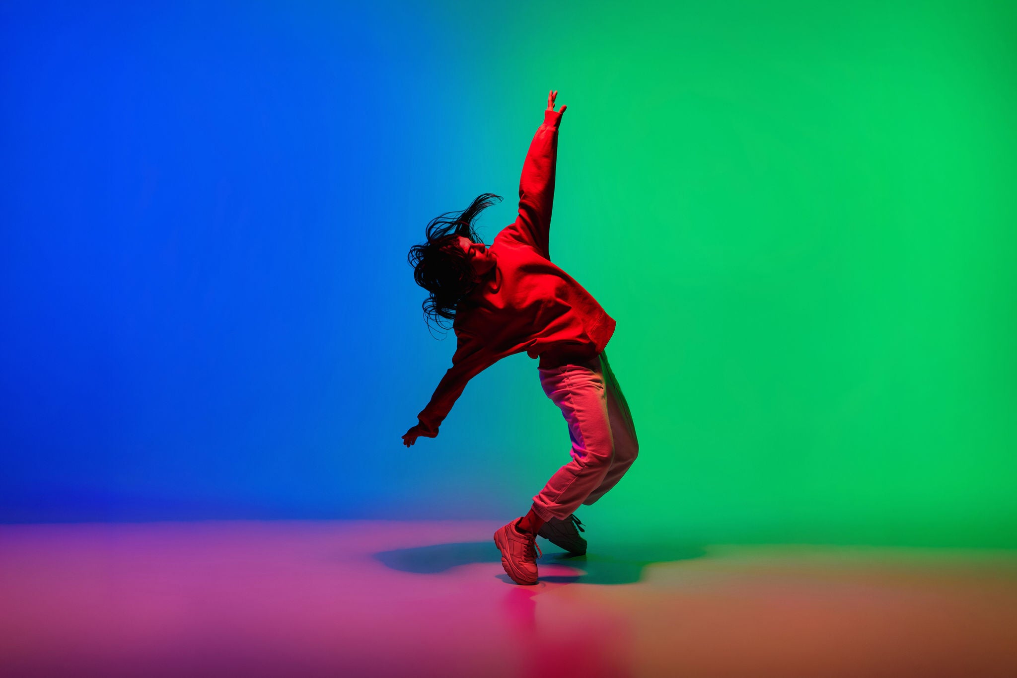 Danser in beweging met zijn linkerhand in de lucht en rechter richting de grond tegen een fel blauw-groene achtergrond