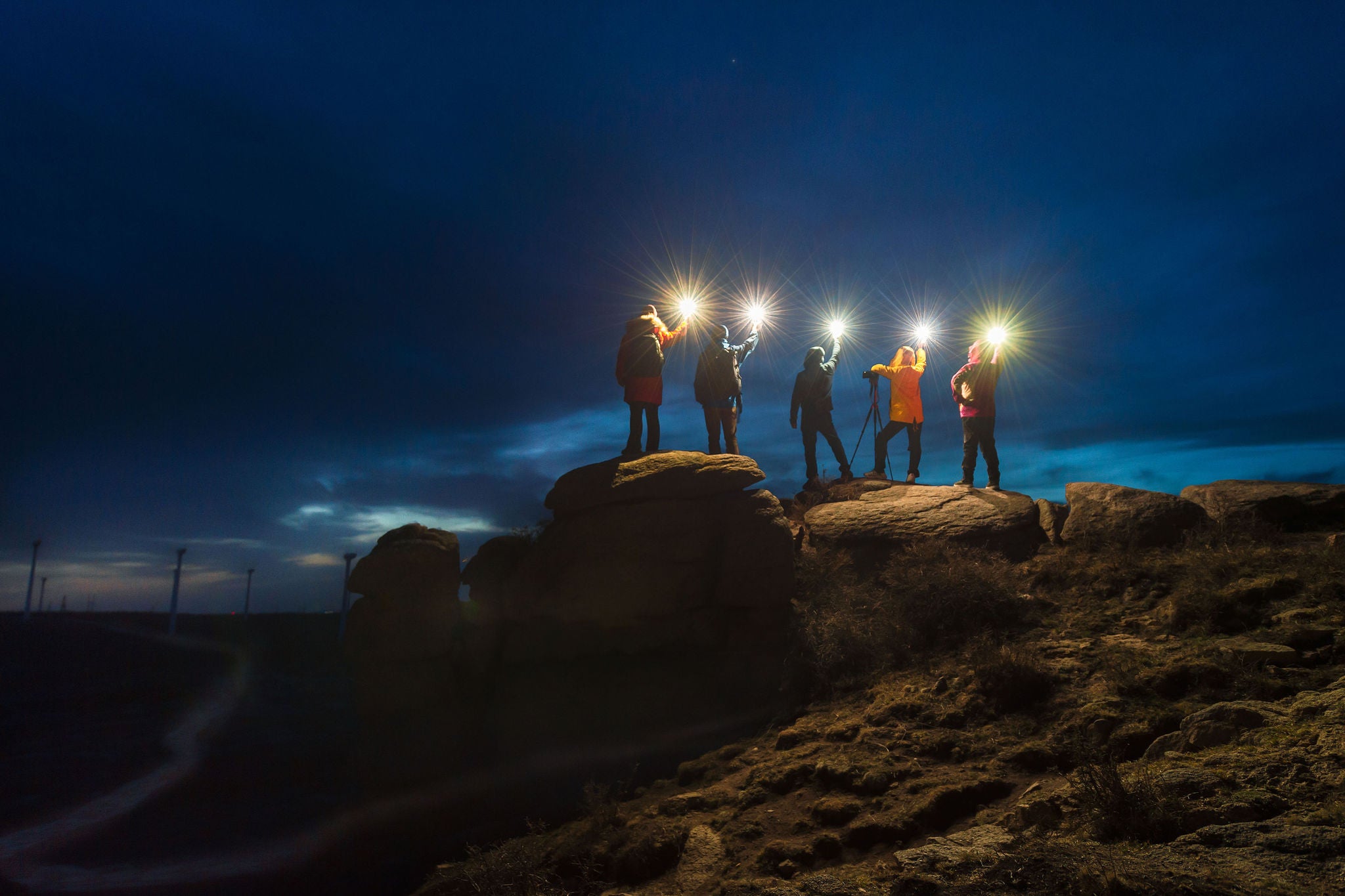 A group of night sky photographers stand on the stone with lamp at night