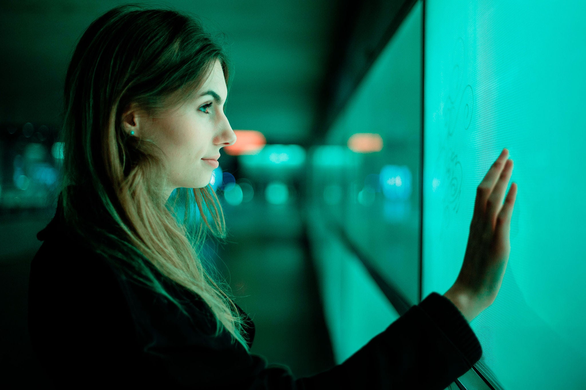 Woman interacts with illuminated digital touchscreen wall.