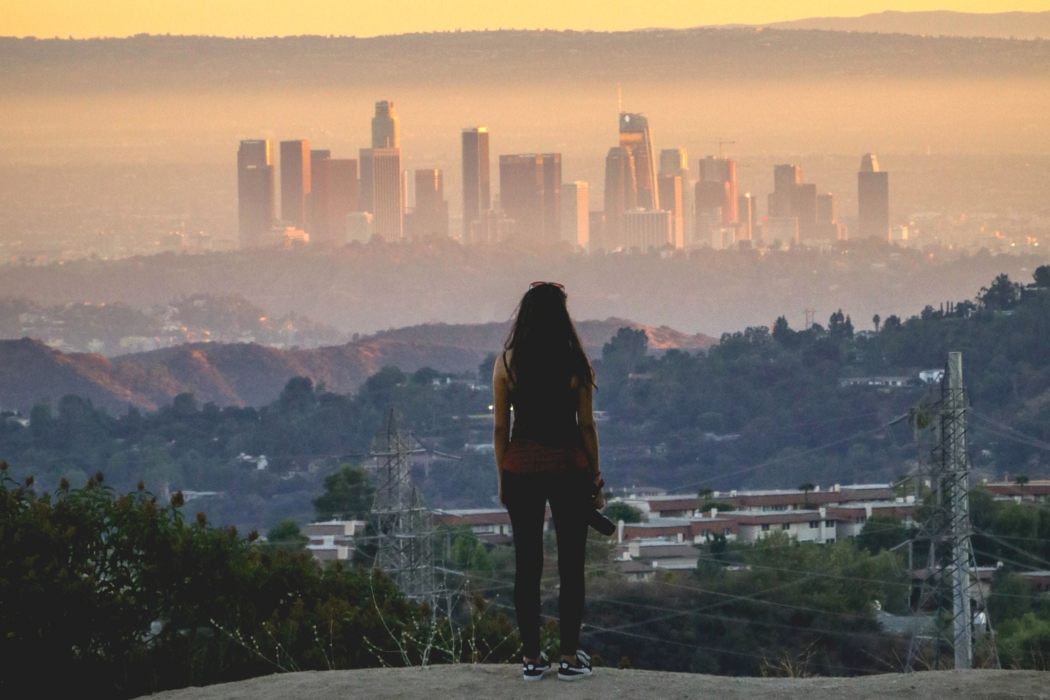 Rear view of a woman standing on a hill overlooking a city skyline at sunset