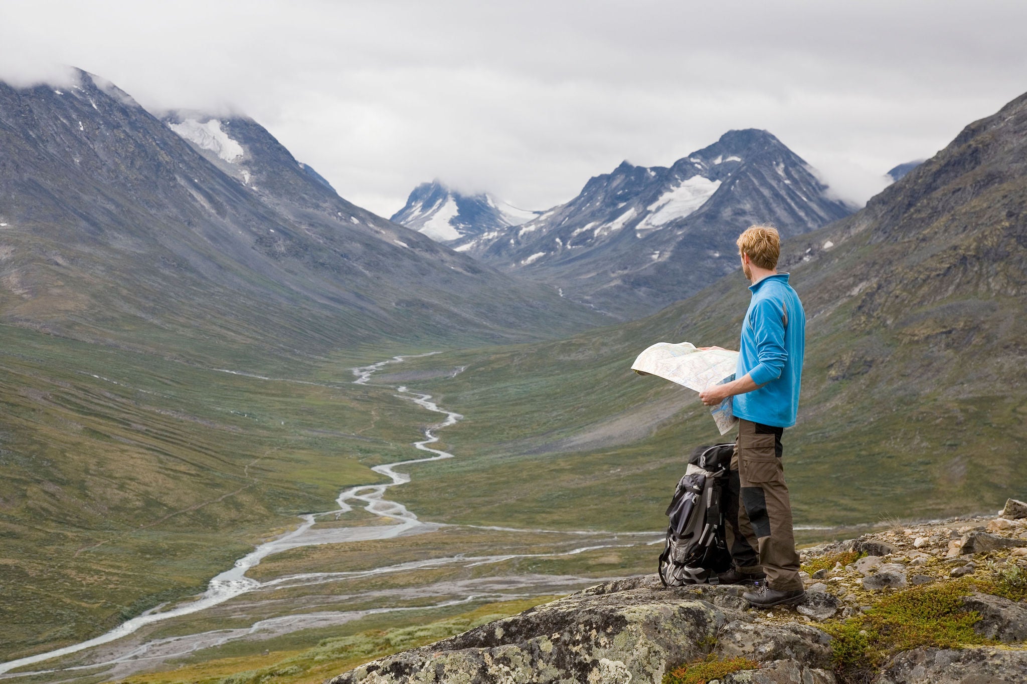 Man holds a map while standing on a rocky hillside overlooking a mountain valley.