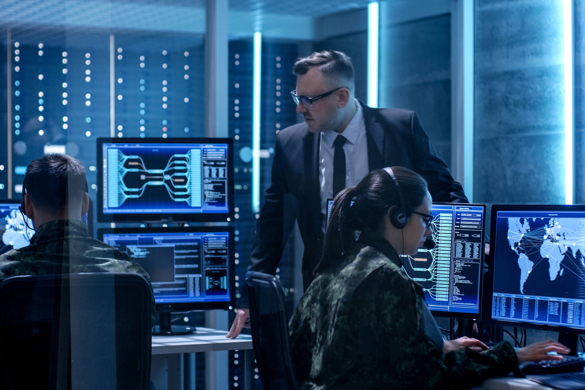 Team of government agents using surveillance in big monitoring room full of computers with animated screens.