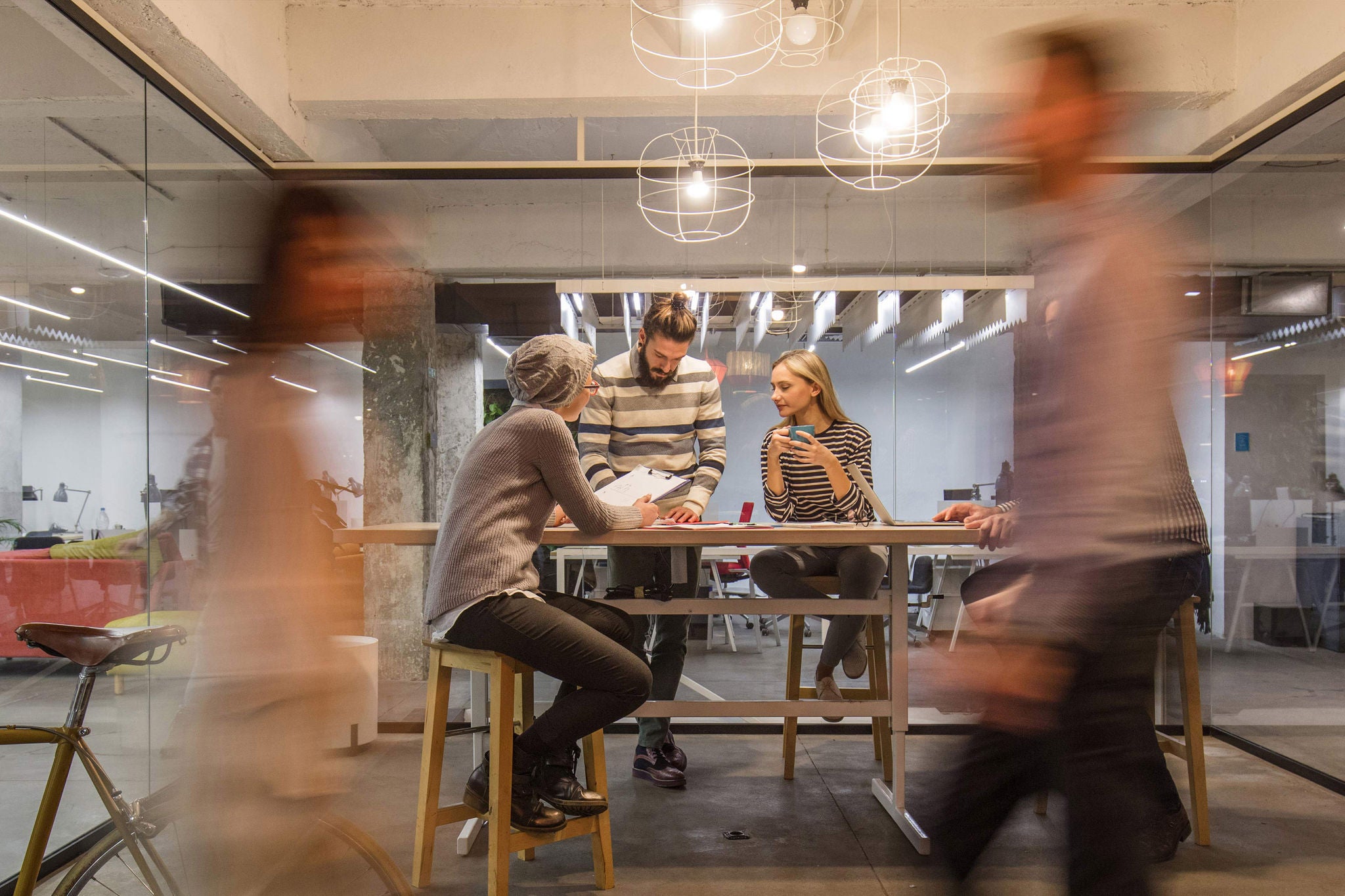 Young entrepreneur having a business meeting inside of an office while their colleagues are walking in blurred motion.