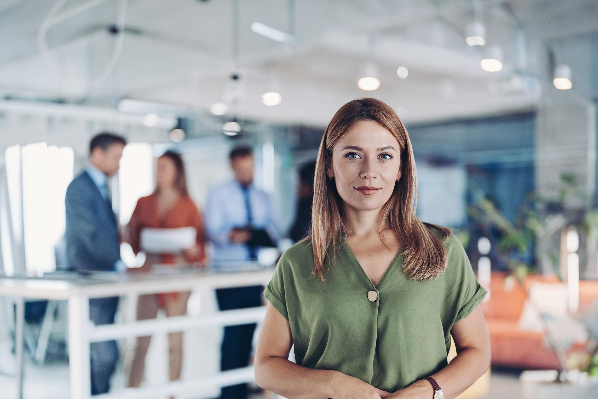 Professional portrait in a modern office with blurred colleagues in background.