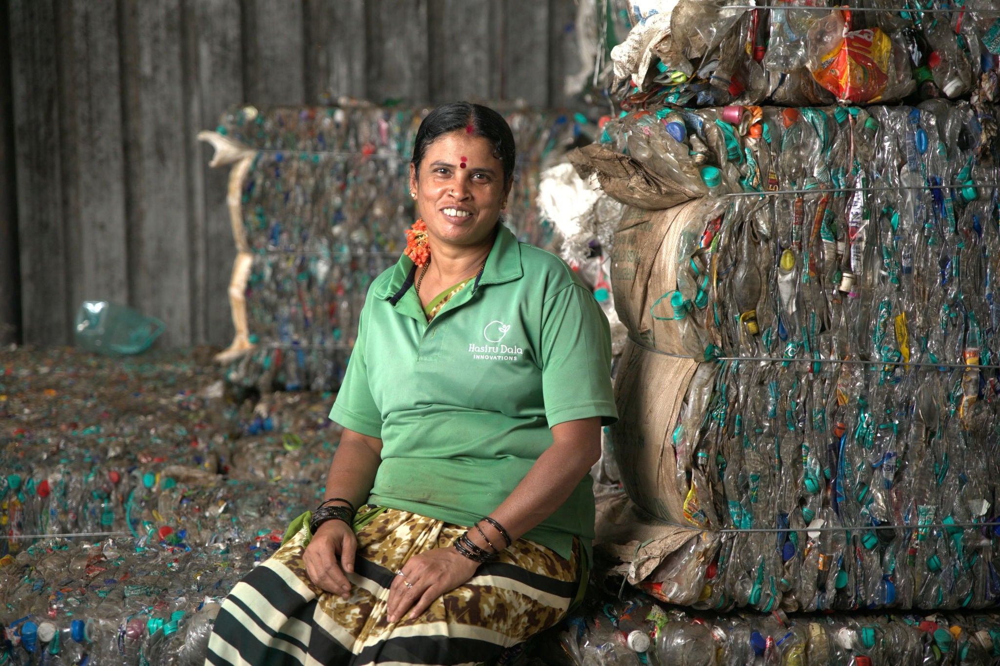 Eine indische Frau mit einem freundlichen Lächeln, gekleidet in ein grünes Shirt, sitzt vor einem gepressten Müllblock