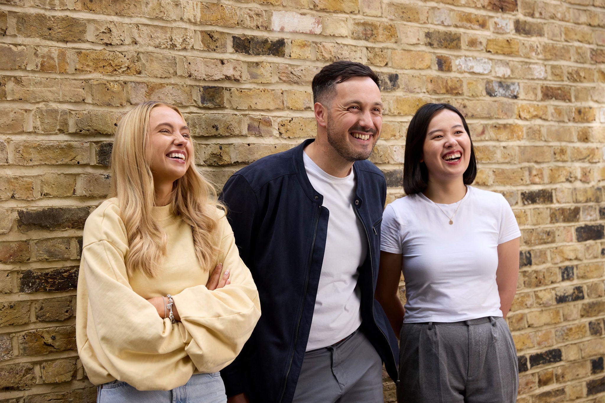 Three colleagues standing together against a brick wall