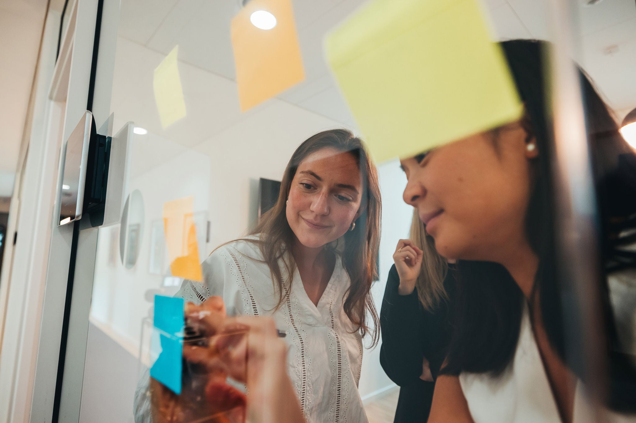 Two young women writing on post-its on glass wall