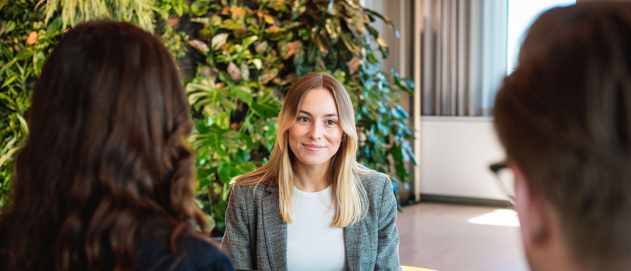 Professionals seated around a table in the EY Stockholm office, discussing work in a meeting area with a green plant wall.