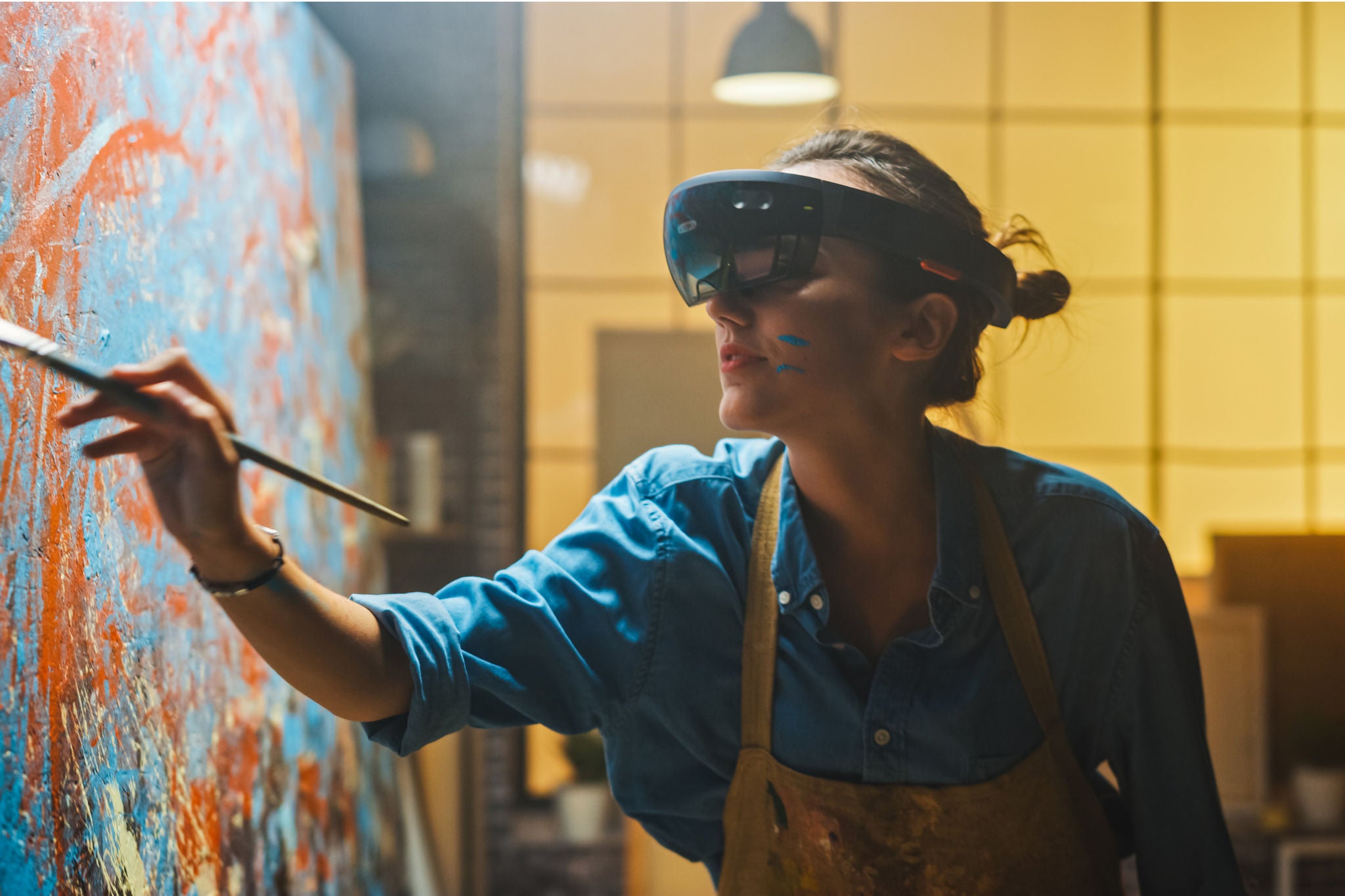 Artist wearing augmented reality headset paints abstract artwork on canvas in a modern studio