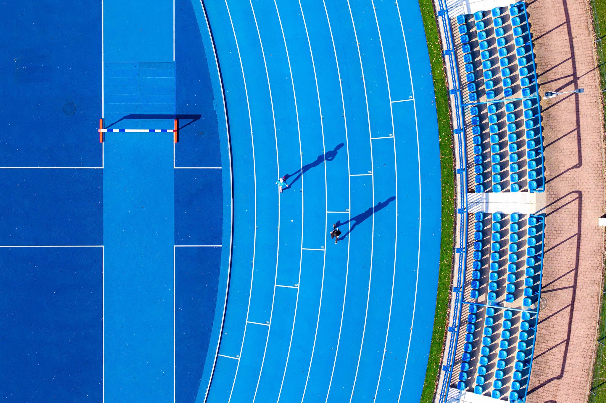 Aerial view of the vivid blue running track curving gracefully beside rows of empty stadium seats, painted in matching hues of blue, Warsaw, Poland.