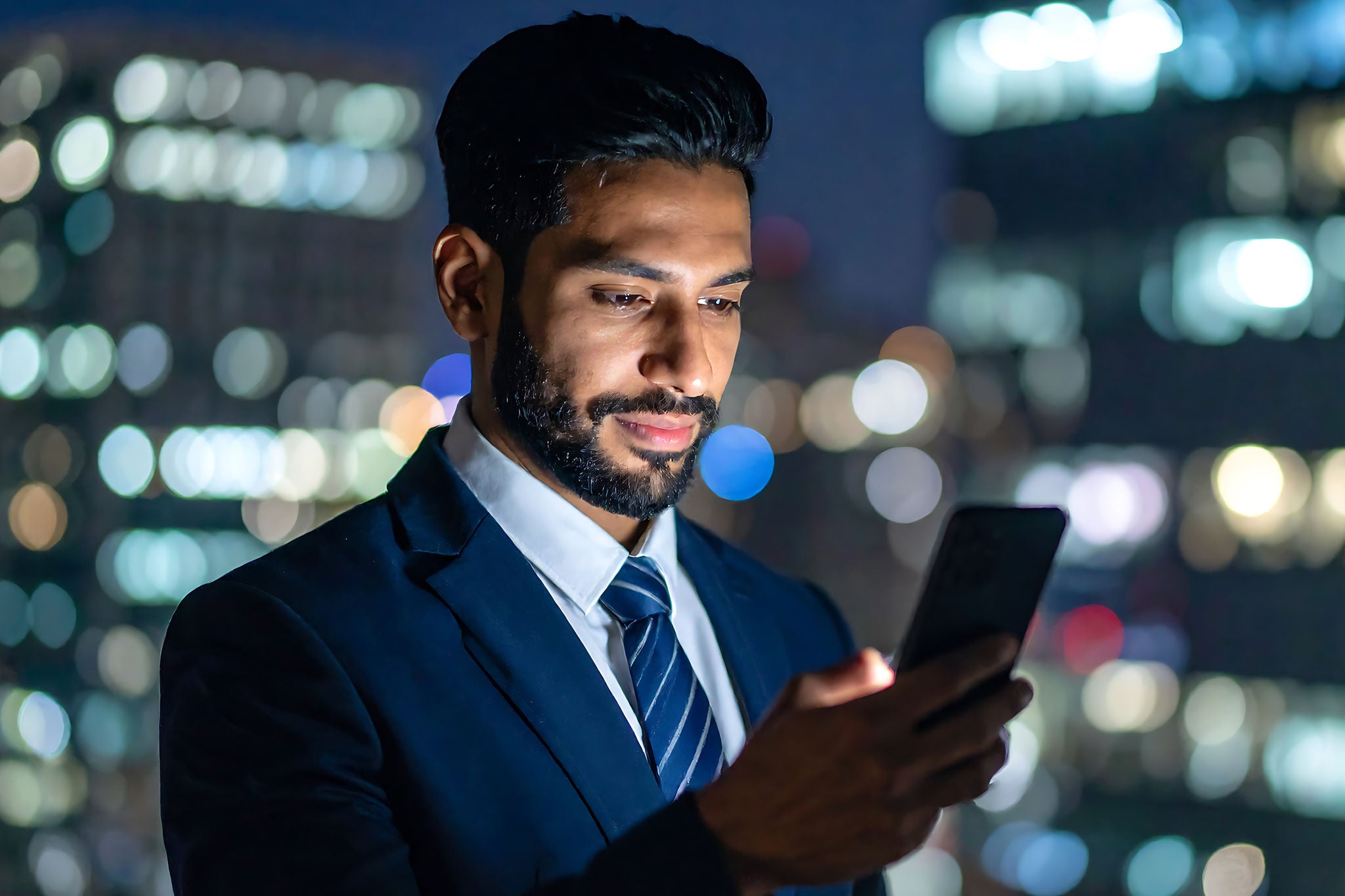 Ein Mann im Anzug blickt in einer städtischen Umgebung auf sein Smartphone