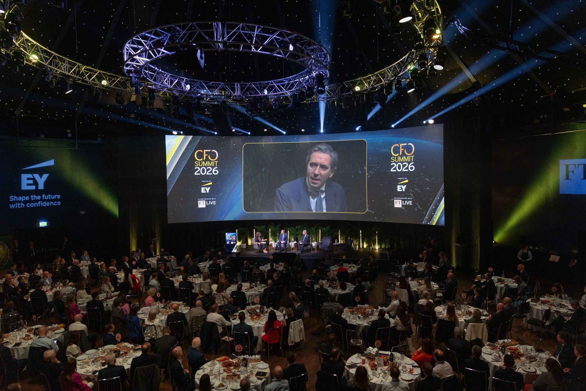 Wide-angle view of the EY CFO Summit 2026, with a panel discussion on stage and attendees seated at round tables.