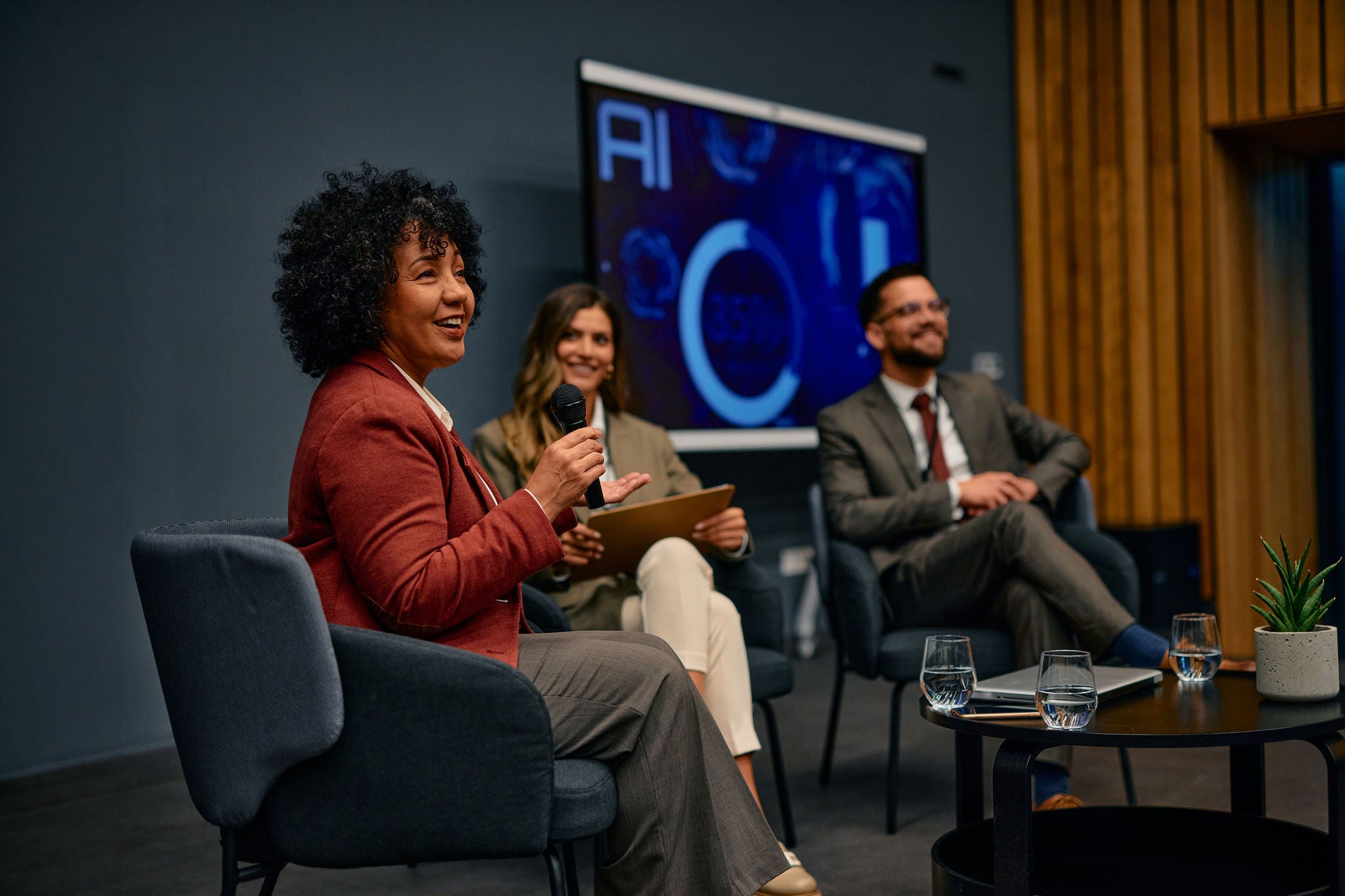 Diverse group of business professionals listening attentively as a businesswoman leads a discussion on artificial intelligence design at a modern conference
