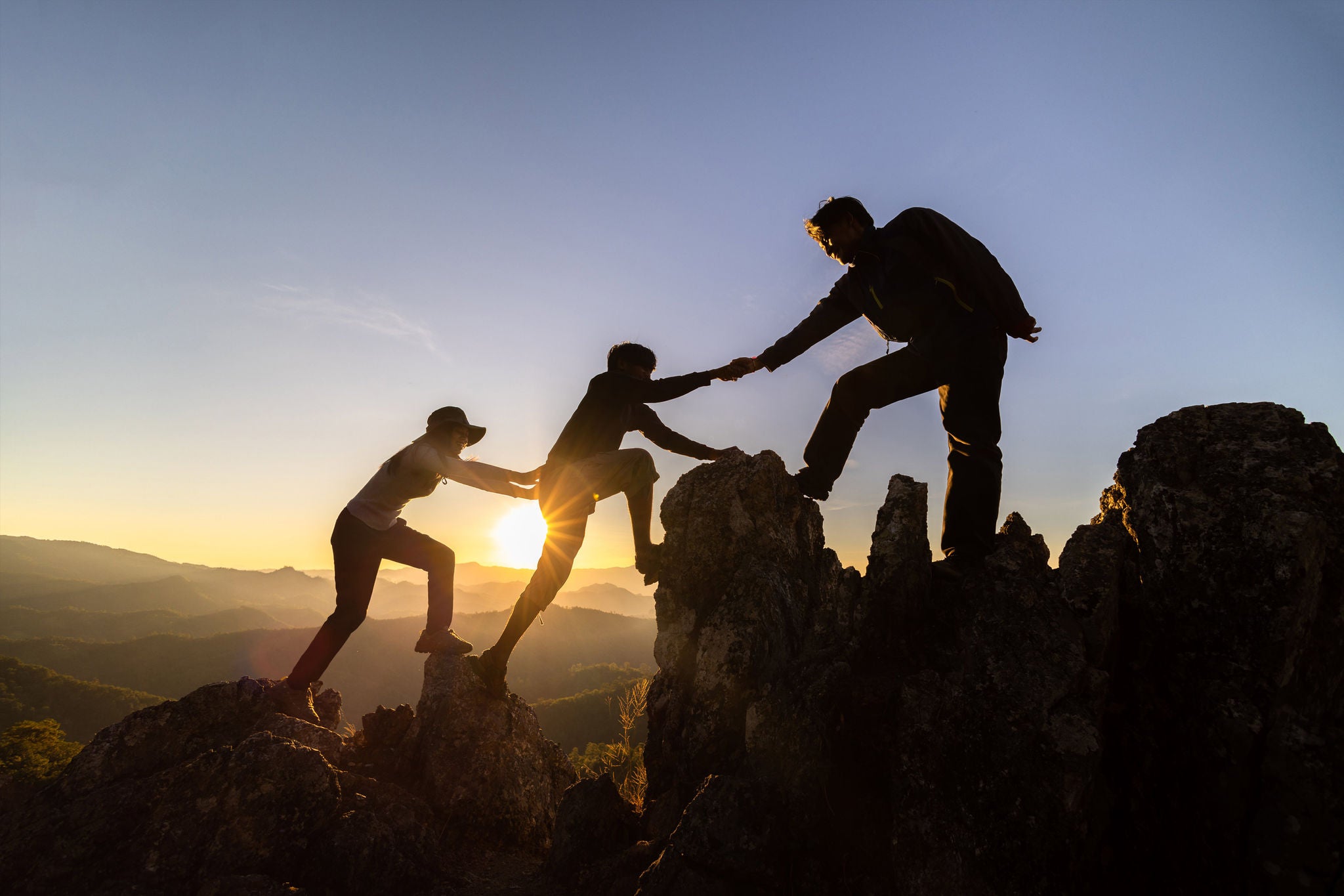 silhouette of Teamwork of three  hiker helping each other on top of mountain climbing team. Teamwork friendship hiking help each other trust assistance silhouette in mountains, sunrise. 