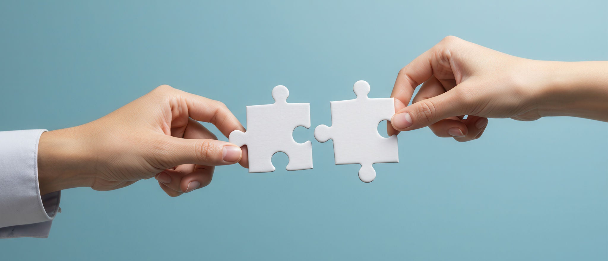 To hender som setter sammen hvite puslespillbiter mot en klar blå bakgrunn
