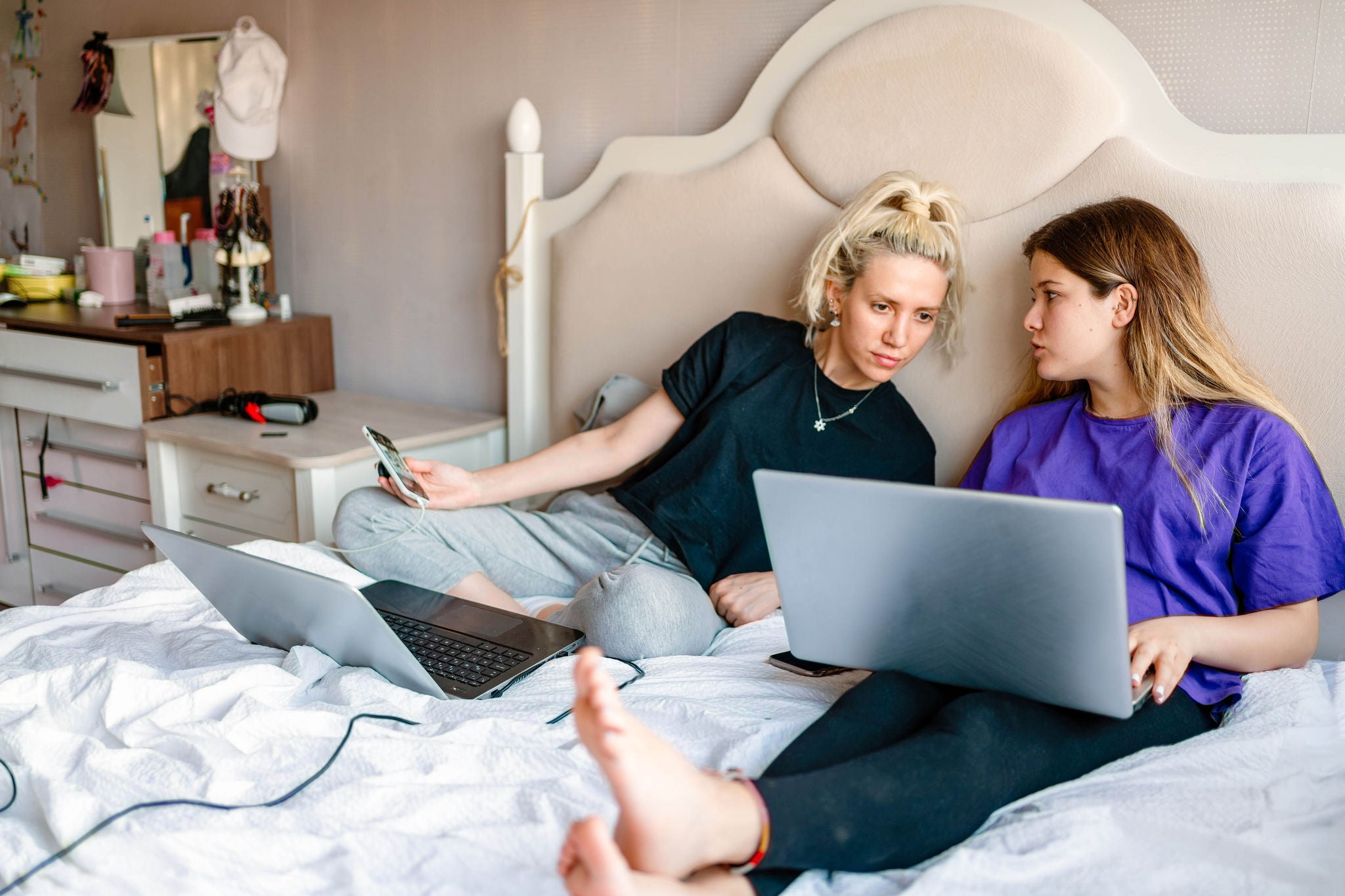 Women using laptop and a smart phone on a bed