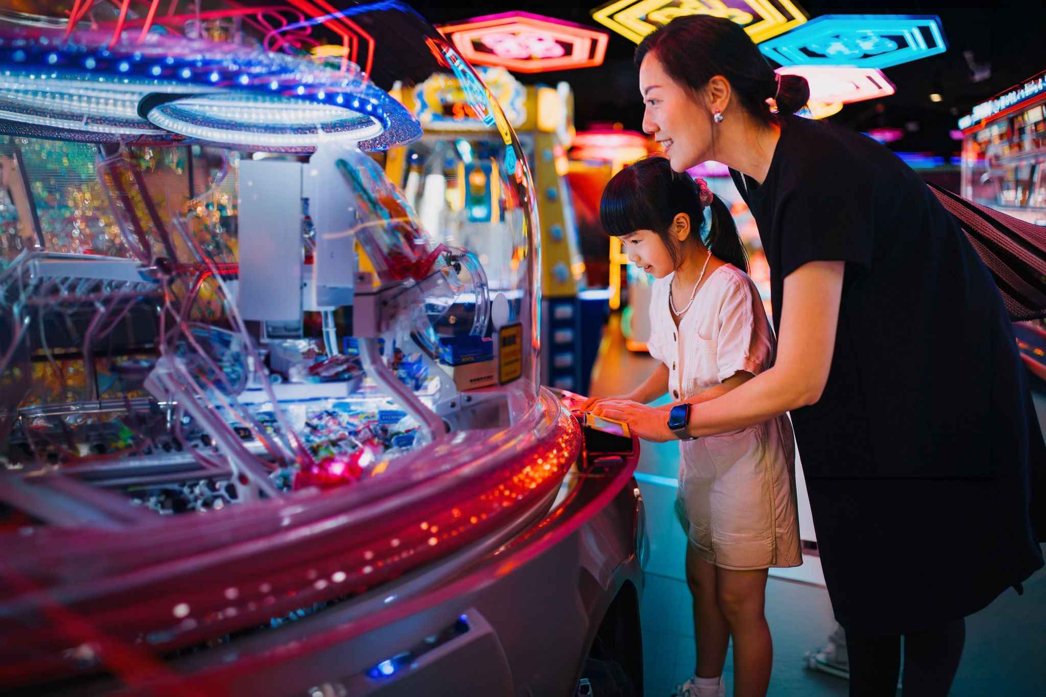Asian mother playing claw machine with her daughter