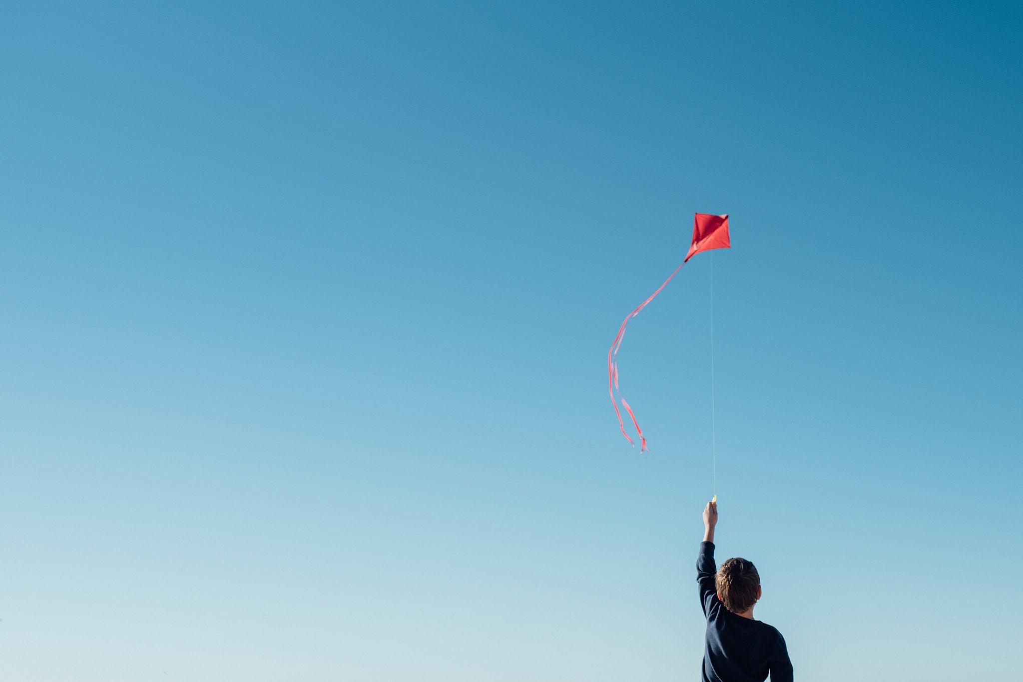 Personne faisant voler un cerf volant rouge dans ciel bleu clair