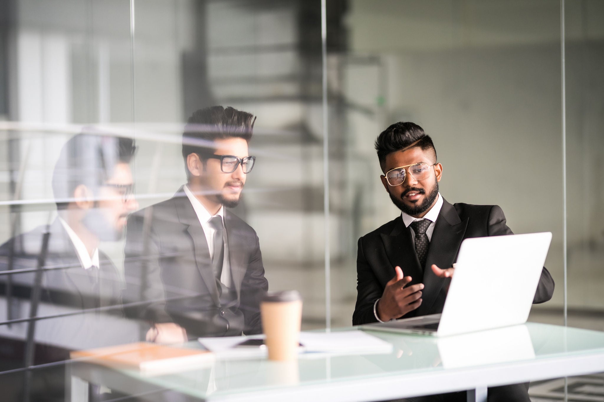 Three indian businessmen working together talking collaborate on laptop in office