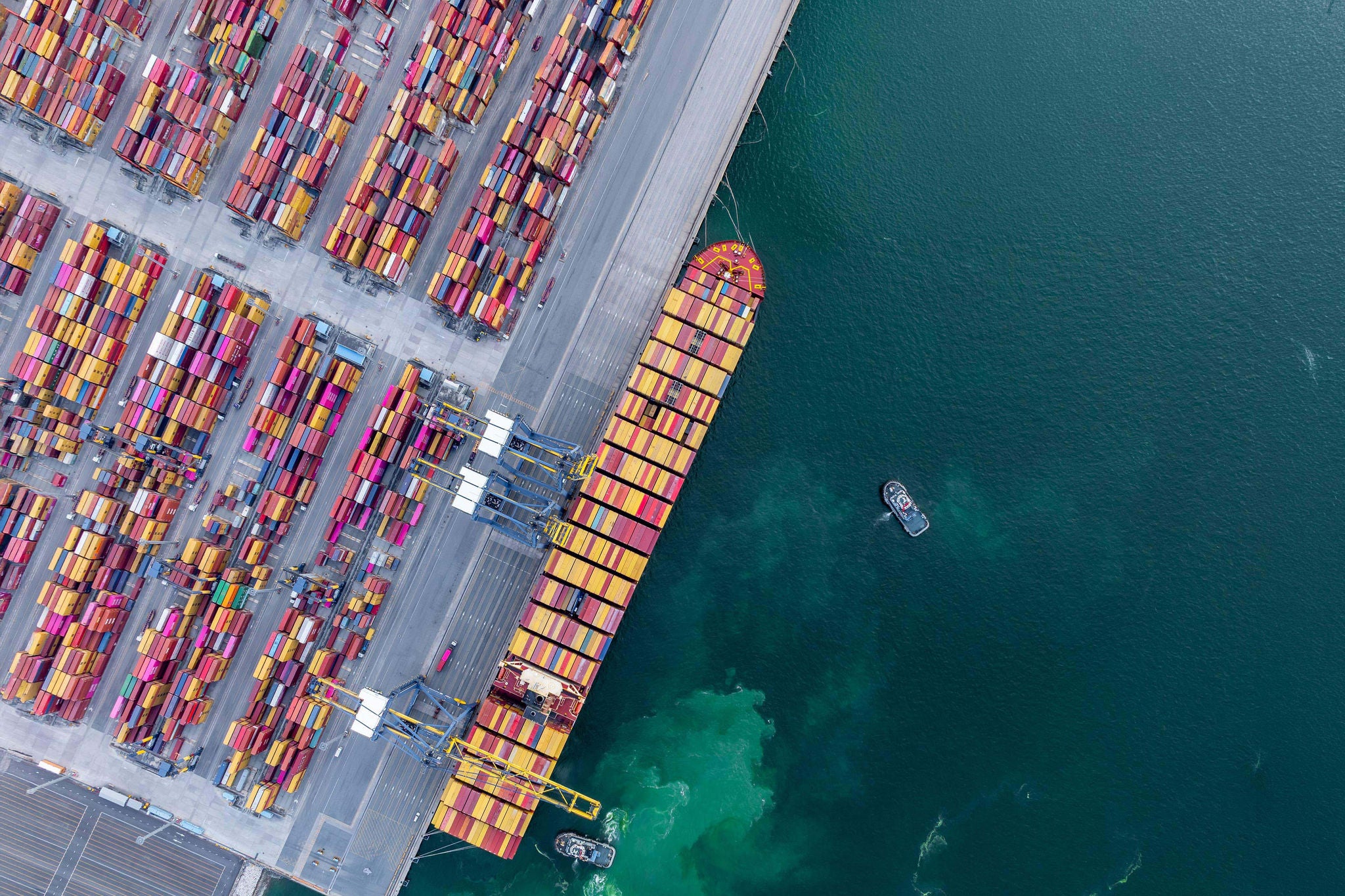 Aerial view of a container ship at deep sea port with tugboat assistance, showing global trade logistics hub