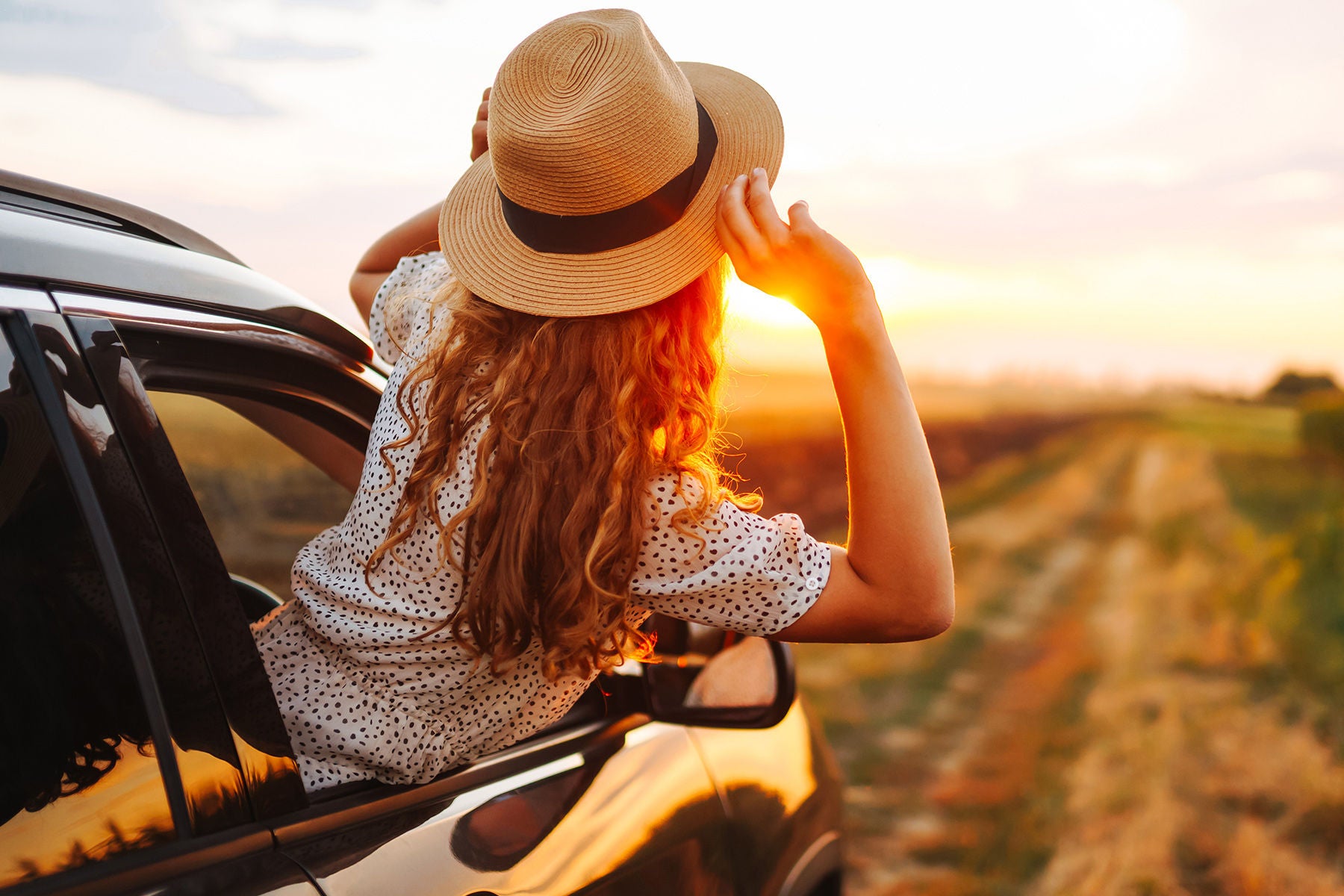 Junge Frau lehnt sich aus dem Auto und genießt den Sonnenuntergang