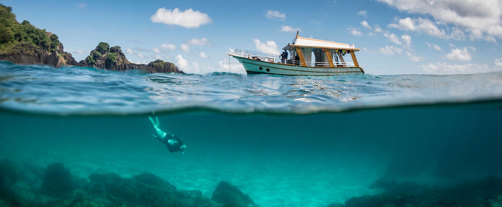 View of a tour boat and a woman free diving at 'Sancho' beach in the archipelago of Fernando de Noronha - Brazil