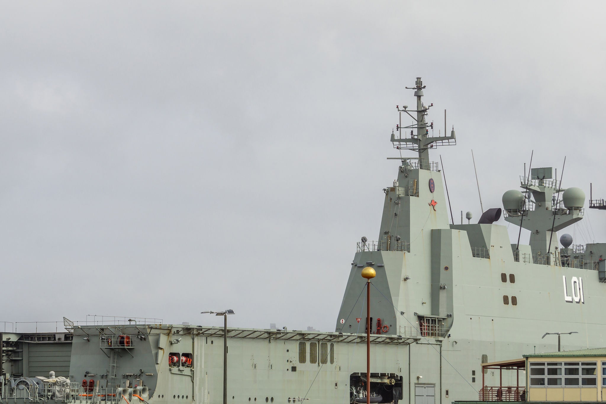 Naval ship docked at a port under cloudy sky