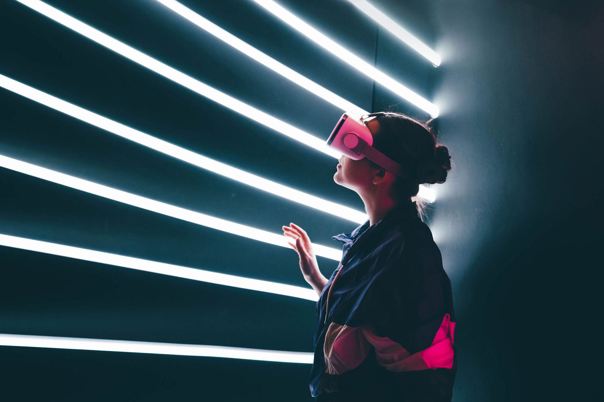 Girl using VR goggles in colorful neon lights, having fun. Wearable virtual augmented reality digital innovation technology concept