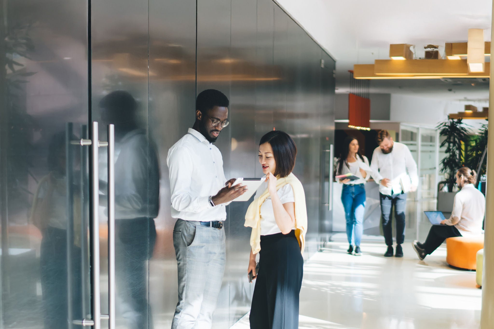 Multiethnic staff in casual clothes walking and standing in big sunlit corridor of modern workspace.