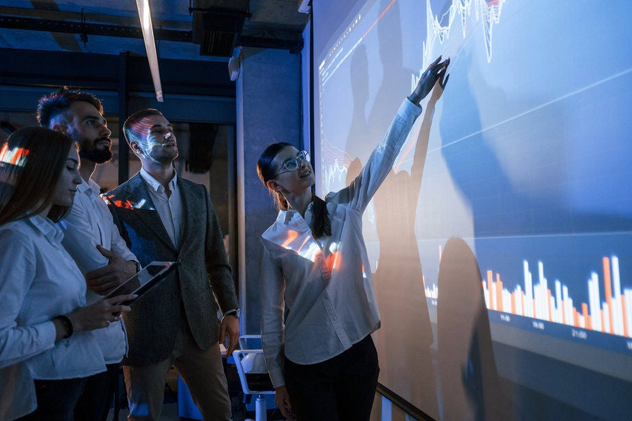 Young Asian woman using smartphone against illuminated digital display in city street at night. Blockchain technology. Trading cryptocurrency.  NFT (Non-Fungible Token) investment.